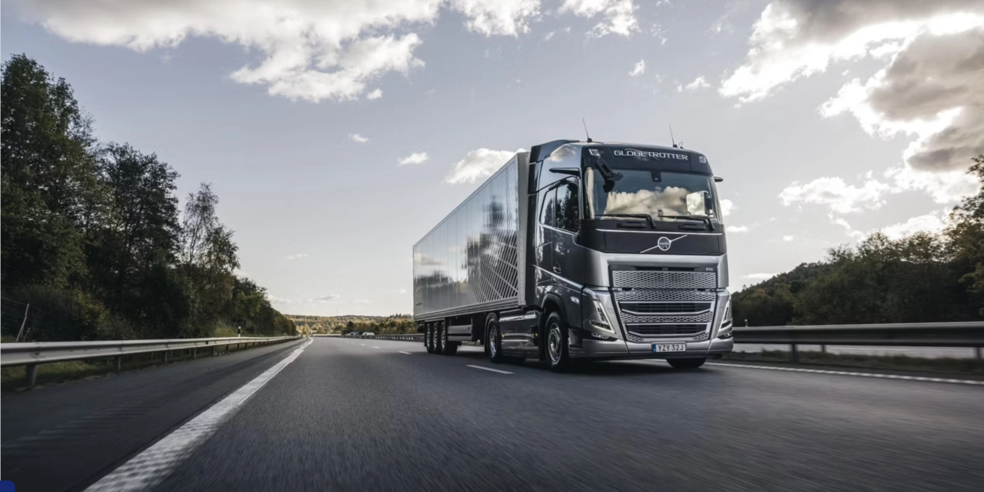 Ein moderner Volvo-Lkw fährt auf einer von Bäumen gesäumten Autobahn unter leicht bewölktem Himmel.