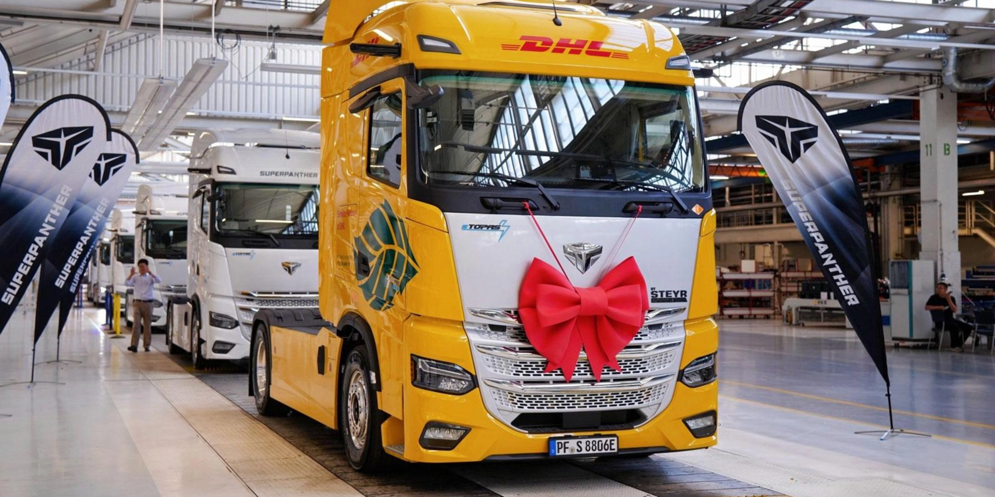 DHL electric truck with a red gift bow displayed inside a production hall.