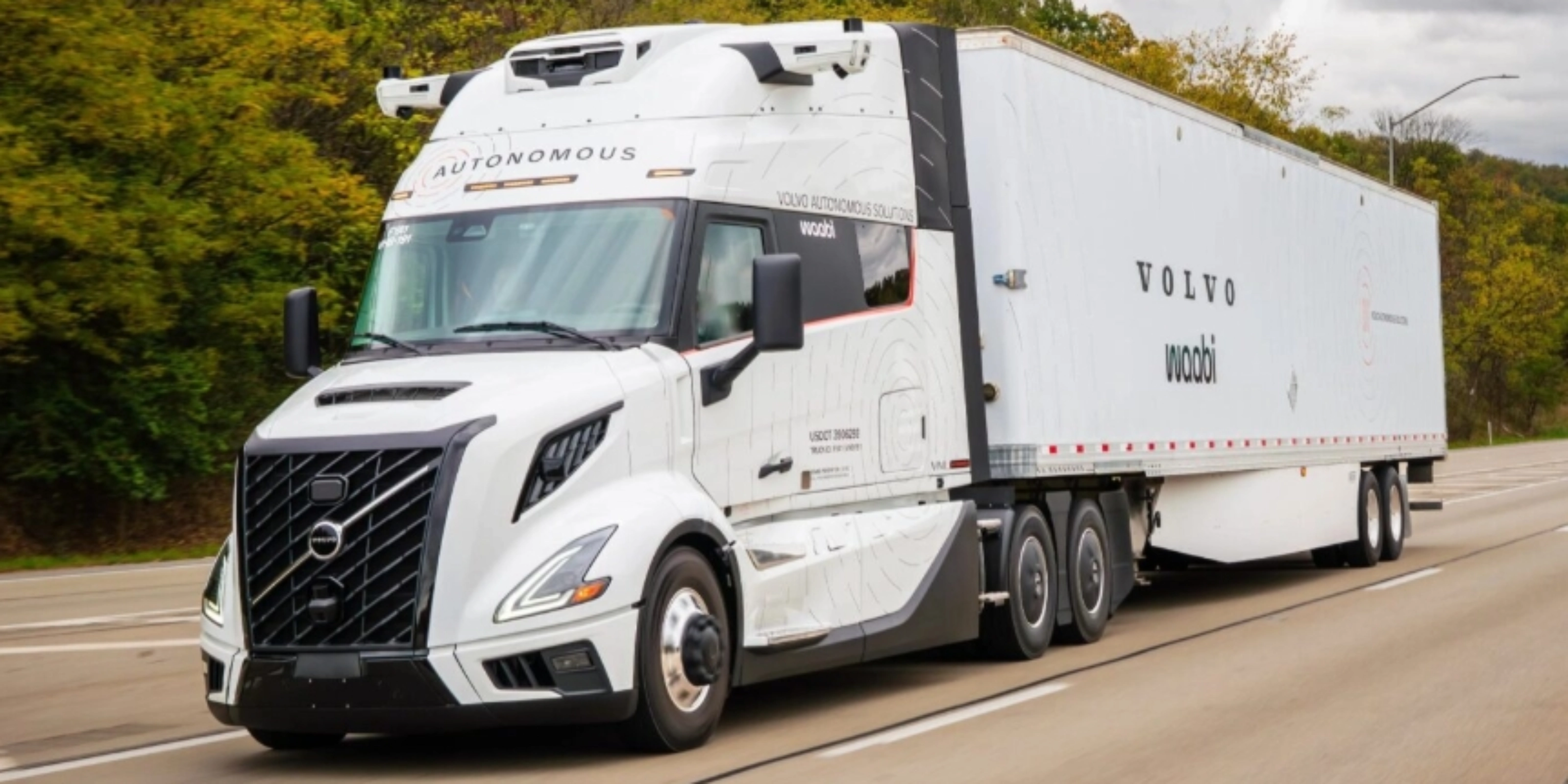 Ein weißer autonomer Volvo-Lkw mit Waabi-Logo fährt auf einer Autobahn an Bäumen vorbei.