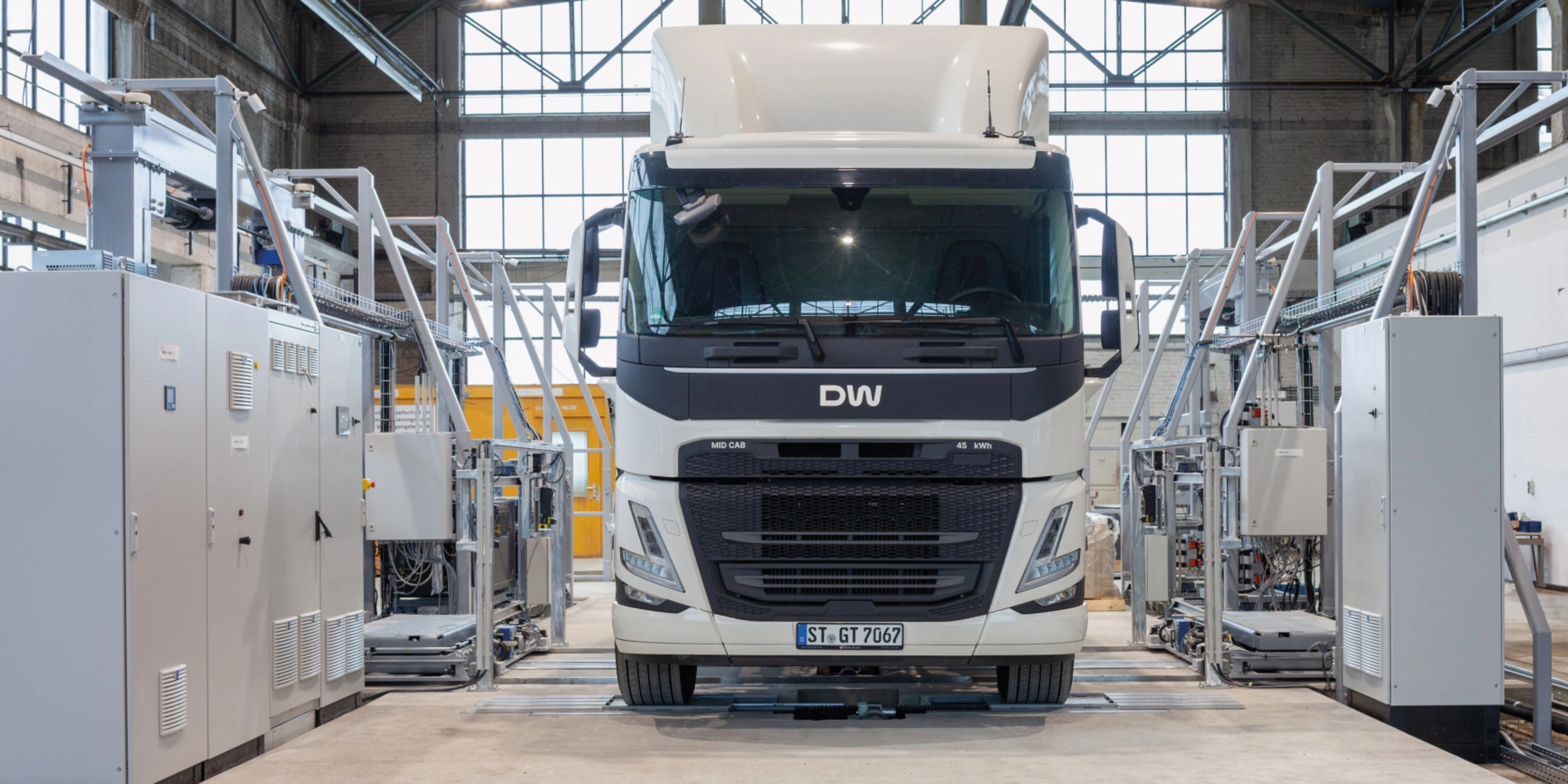 Electric truck in a test hall, surrounded by technical equipment and control cabinets.