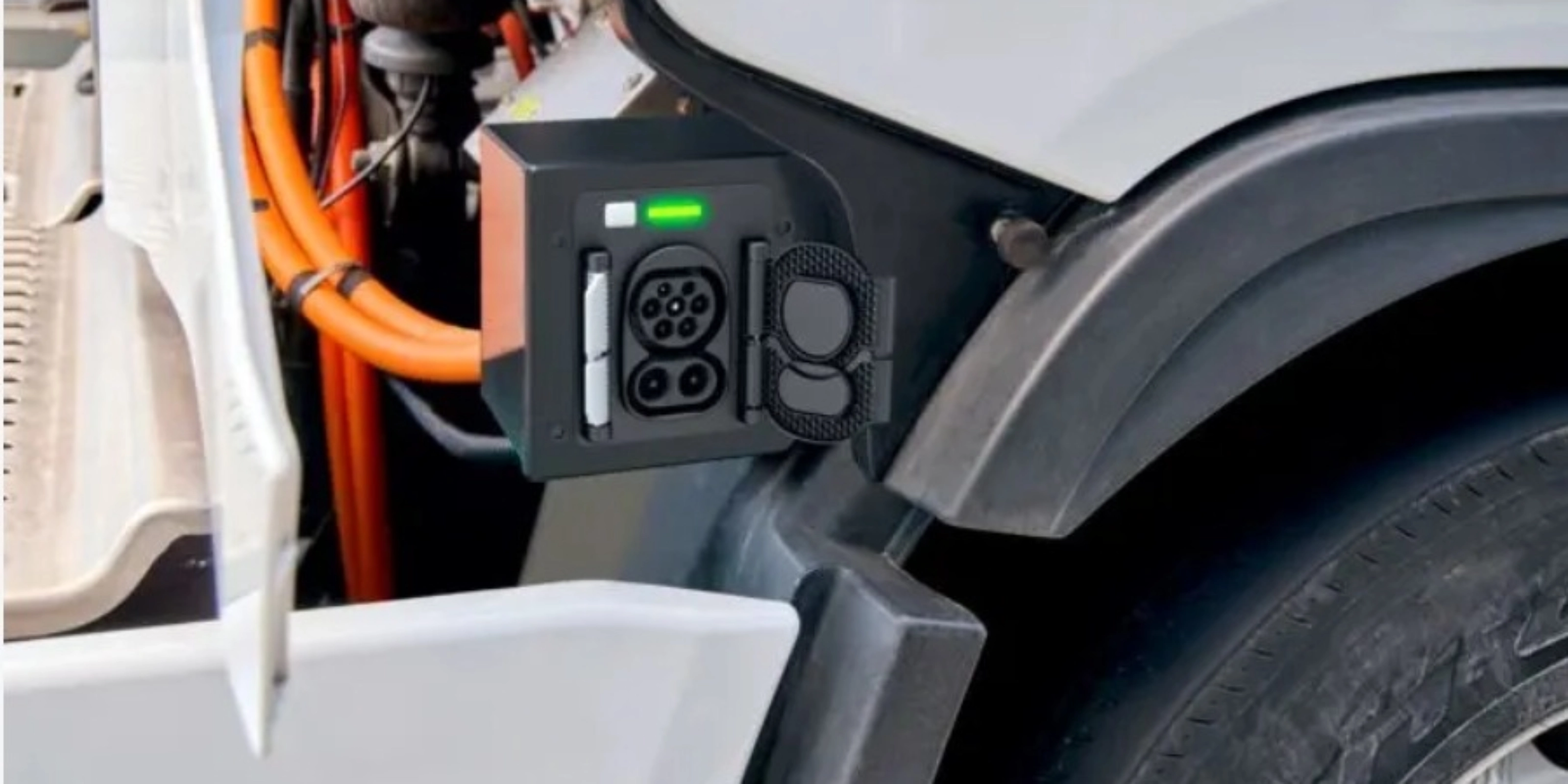 Charging port of an electric truck with visible high-voltage cables and a green status light.