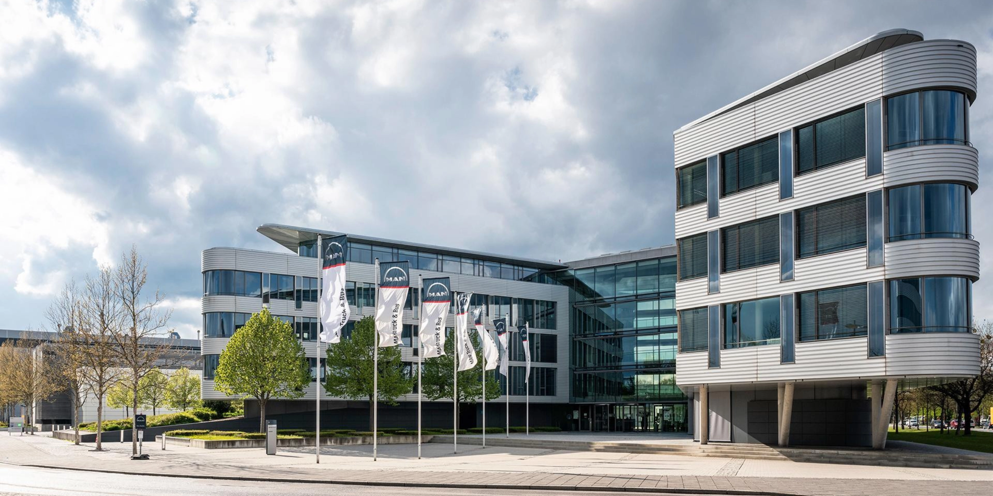 Modern office building with glass facade and MAN Truck & Bus flags in front.