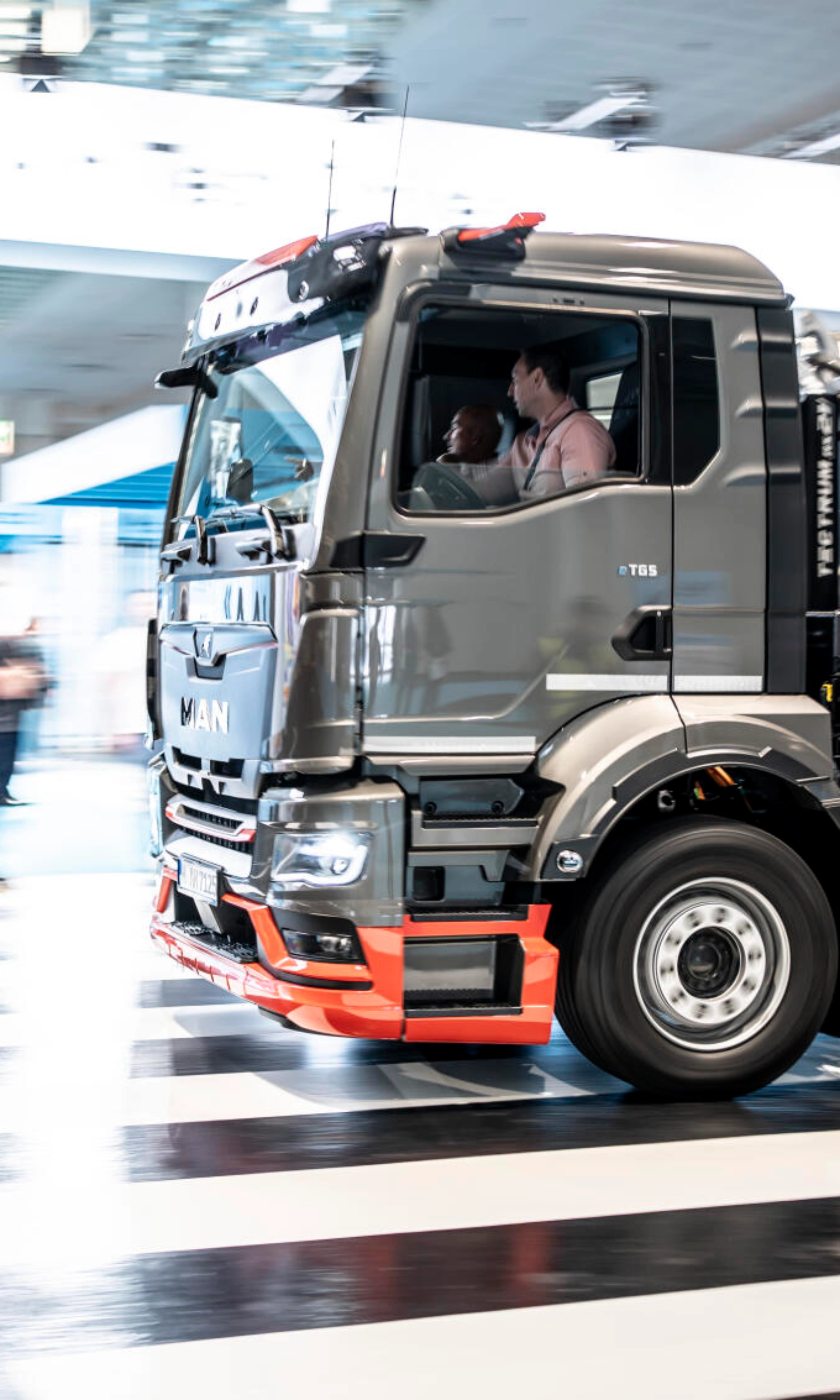 Ein MAN-Lkw fährt mit Bewegungsunschärfe durch ein Testgelände in einer Halle und überquert einen Zebrastreifen.