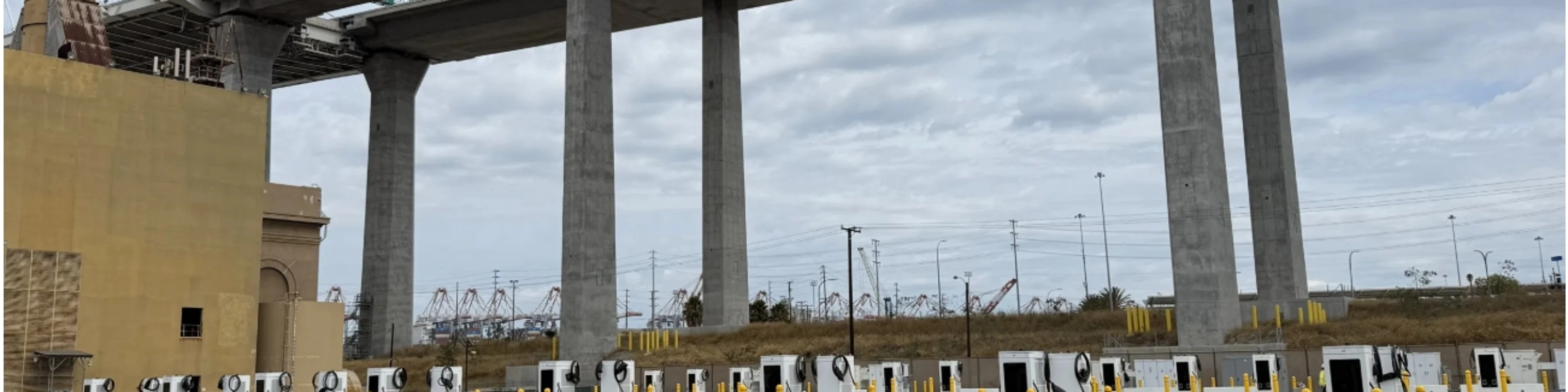 Mehrere E-Ladestationen auf einem Parkplatz unter einer Autobahnbrücke.