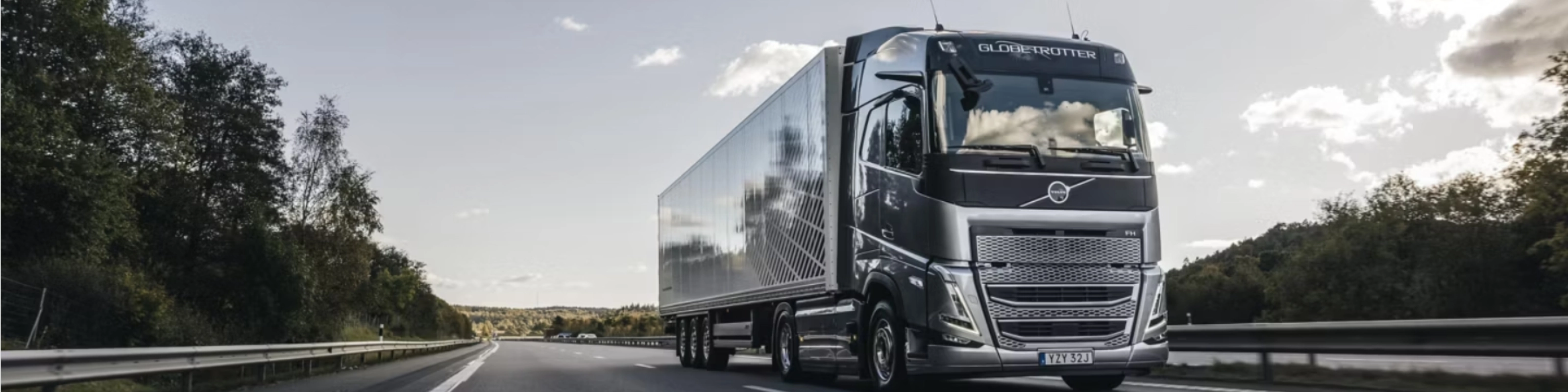 Ein moderner Volvo-Lkw fährt auf einer von Bäumen gesäumten Autobahn unter leicht bewölktem Himmel.