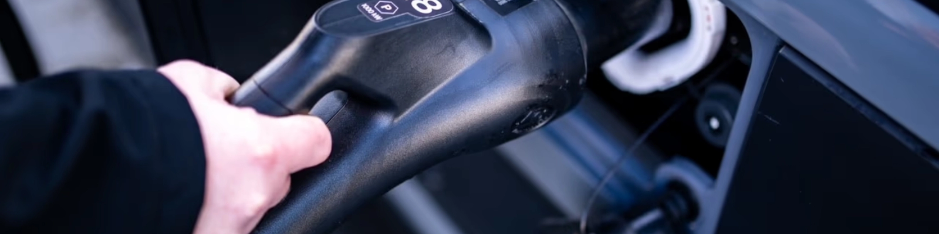A person plugs a charging connector into the charging port of a vehicle.