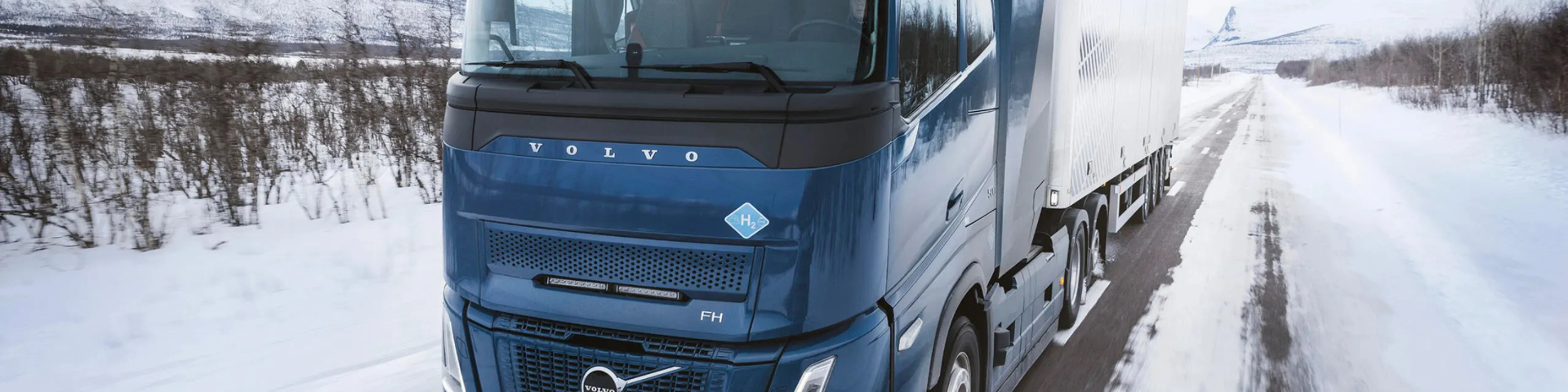 Wasserstoffbetriebener Volvo-Lkw fährt auf verschneiter Straße durch Winterlandschaft.