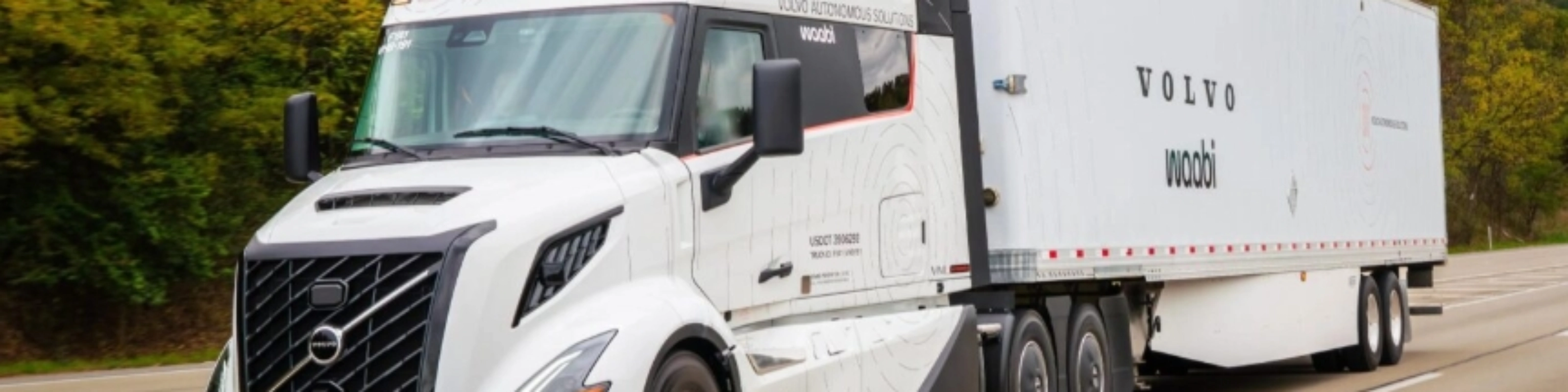 Ein weißer autonomer Volvo-Lkw mit Waabi-Logo fährt auf einer Autobahn an Bäumen vorbei.