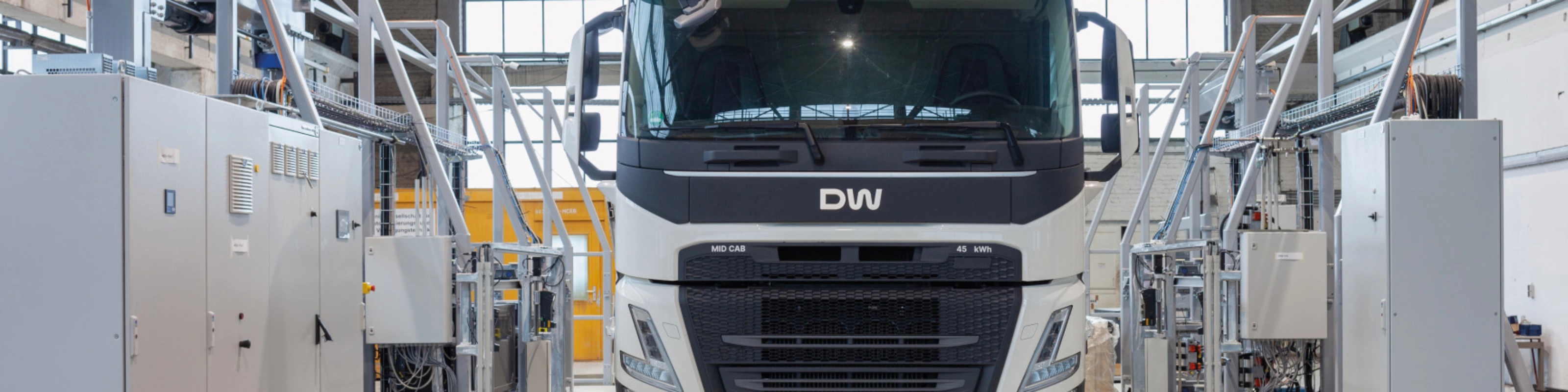 Electric truck in a test hall, surrounded by technical equipment and control cabinets.