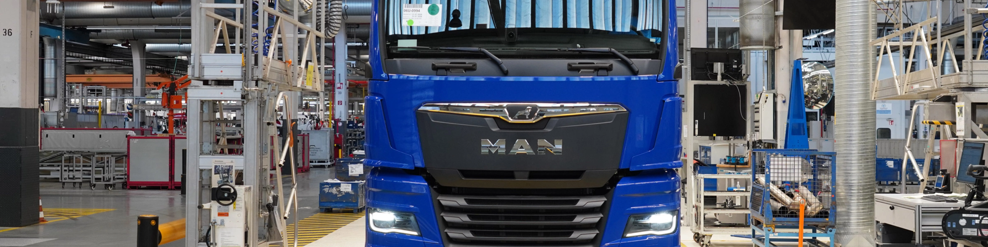 Blauer MAN-Lkw auf einer Produktionslinie in einer modernen Fertigungshalle.