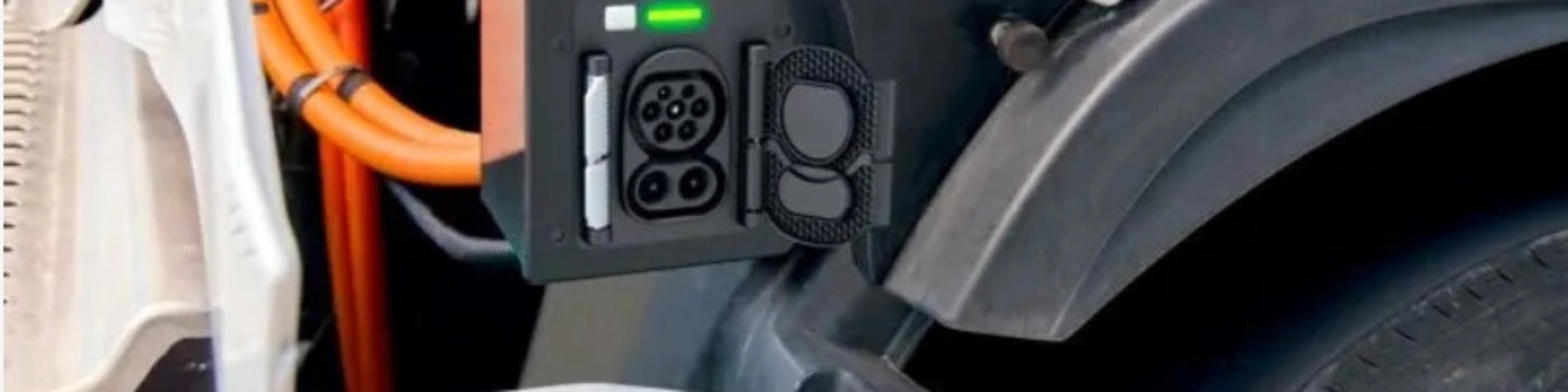 Charging port of an electric truck with visible high-voltage cables and a green status light.