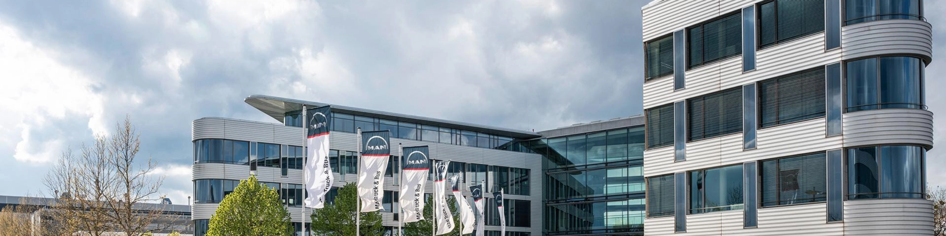 Modern office building with glass facade and MAN Truck & Bus flags in front.