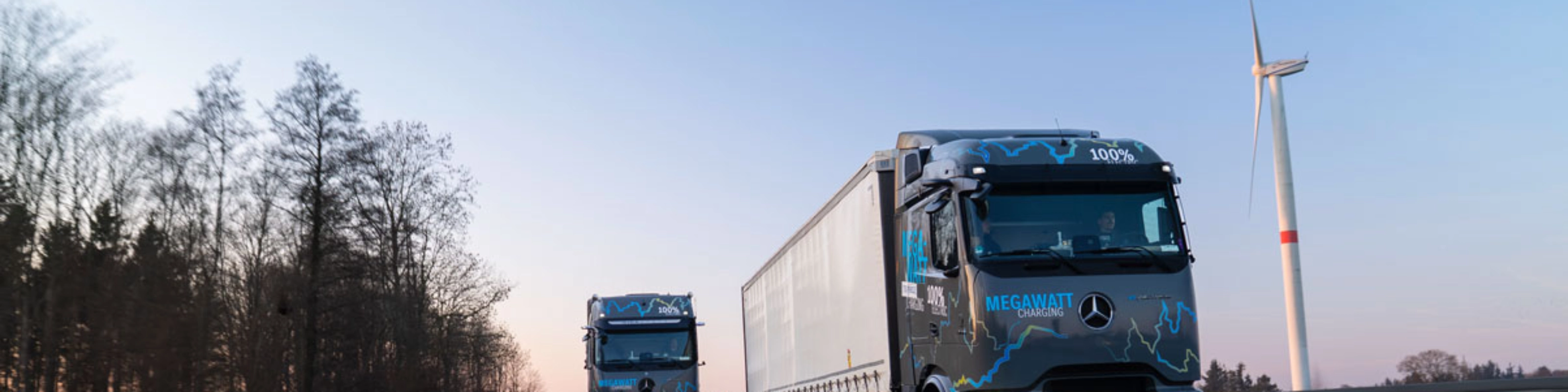 Zwei elektrische Mercedes-Benz-Lkw mit „Megawatt Charging“-Aufschrift fahren bei Dämmerung auf der Autobahn.