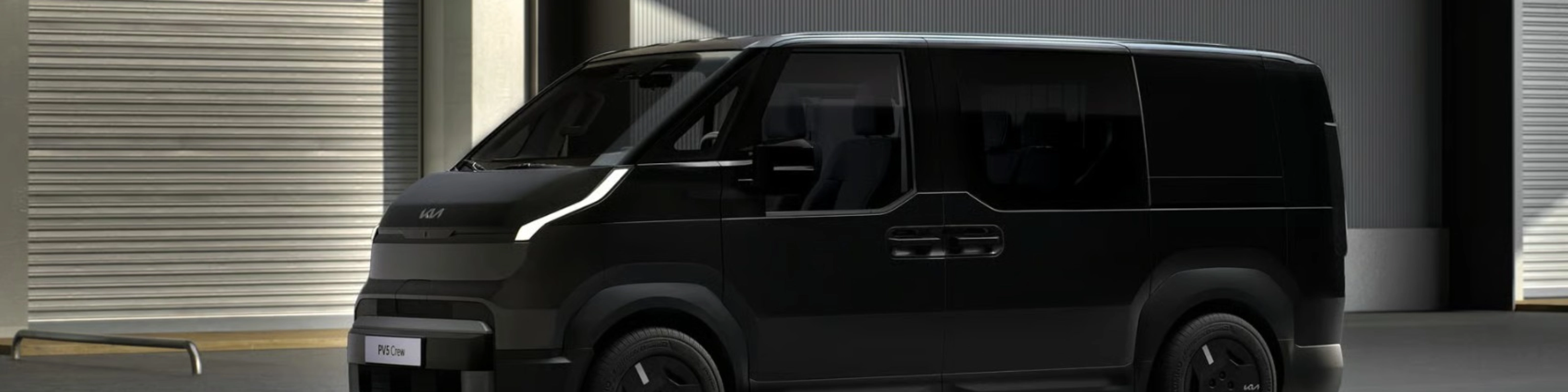 Schwarzer Kia-Van steht vor Industriegebäuden mit geschlossenen Rolltoren.