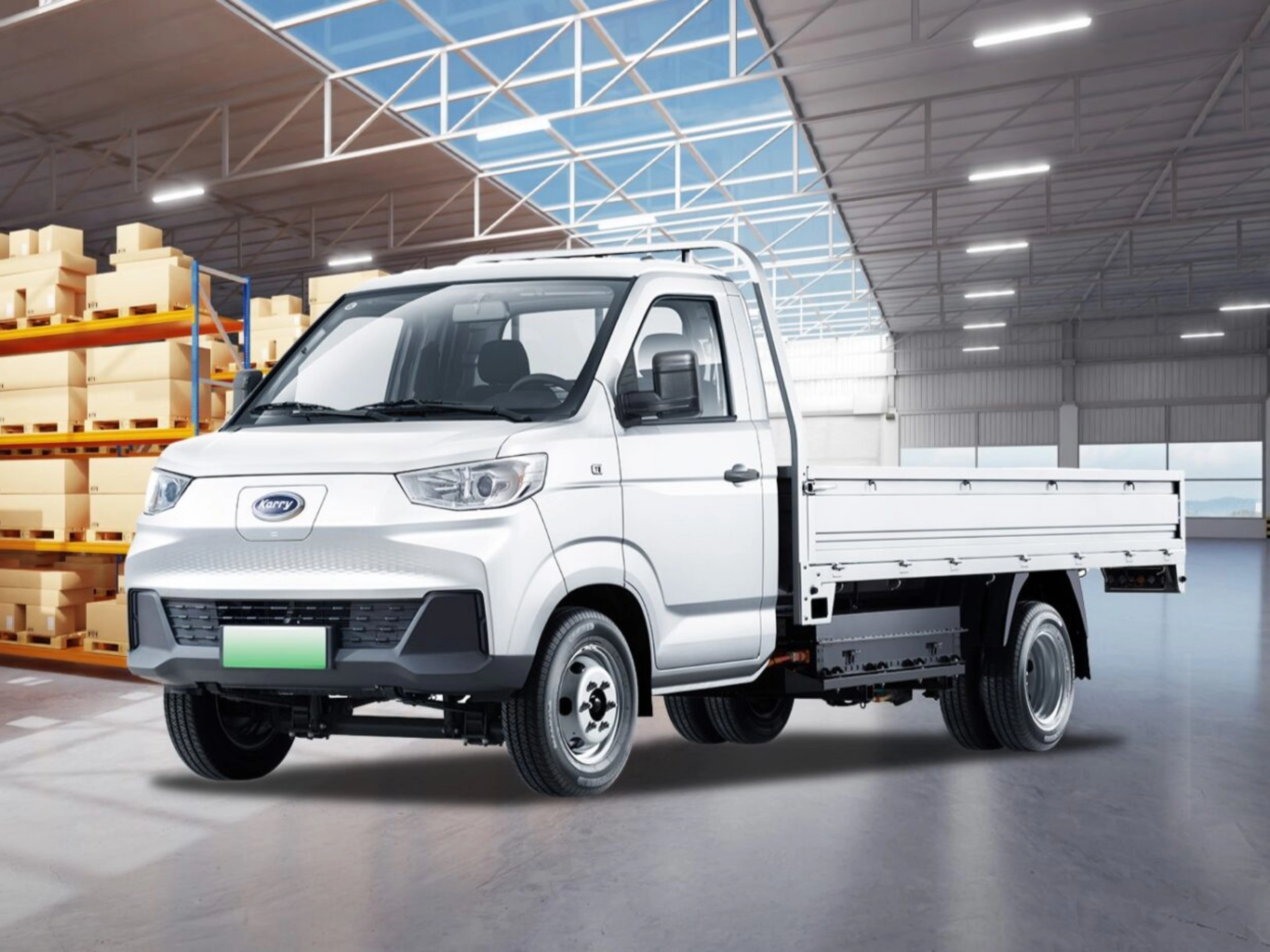 A white Karry electric flatbed truck is parked inside a warehouse near stacked boxes.