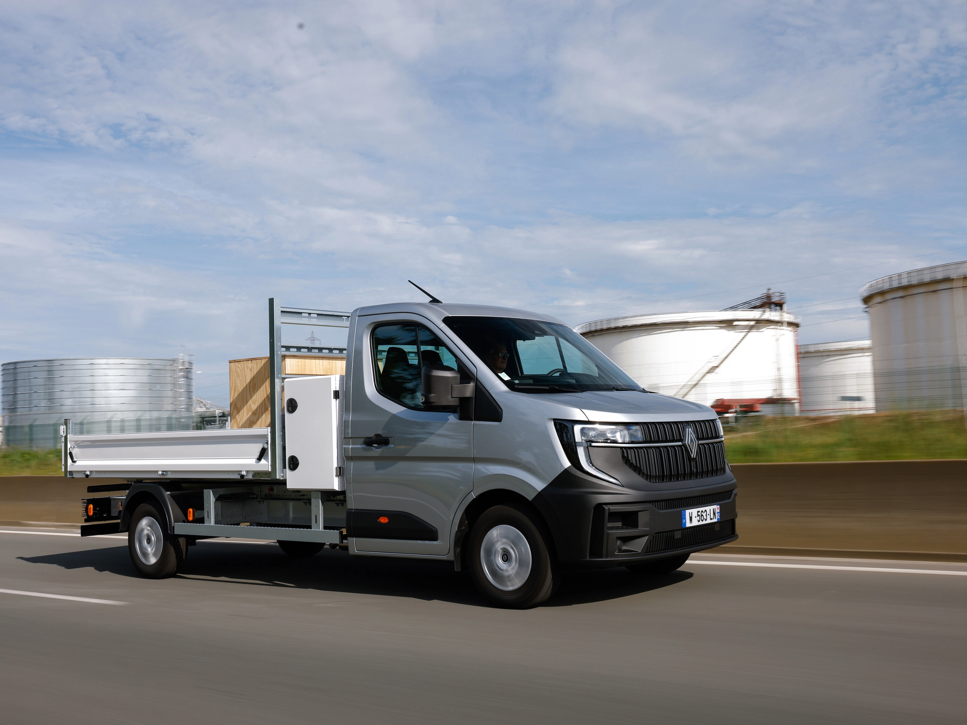 Grey Renault flatbed truck driving on a road in an industrial area.