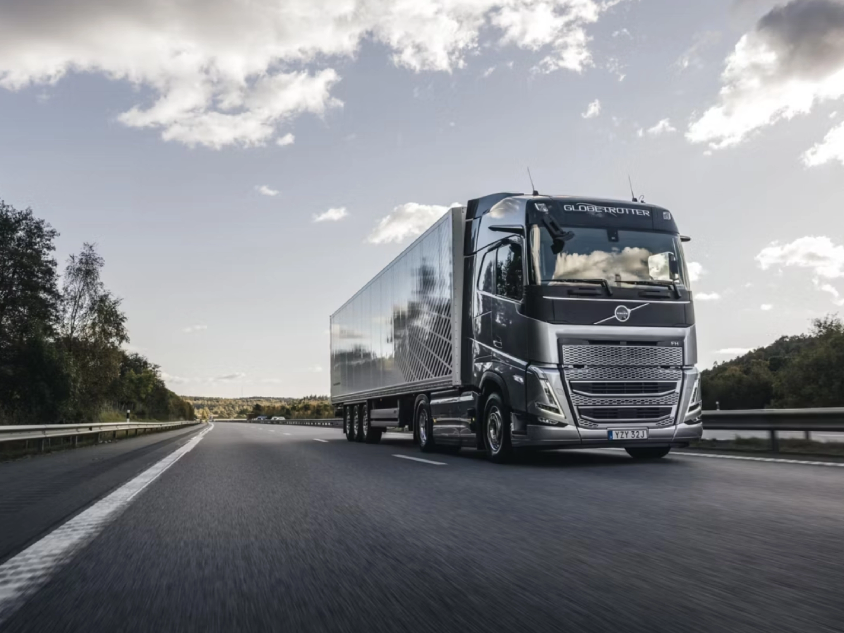 Ein moderner Volvo-Lkw fährt auf einer von Bäumen gesäumten Autobahn unter leicht bewölktem Himmel.