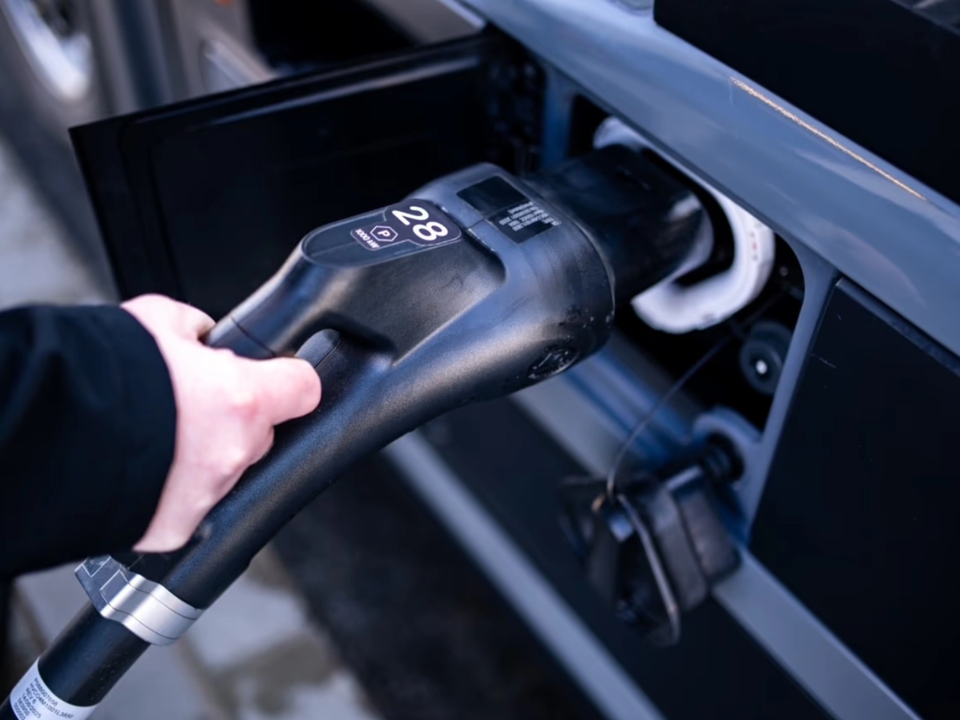 A person plugs a charging connector into the charging port of a vehicle.