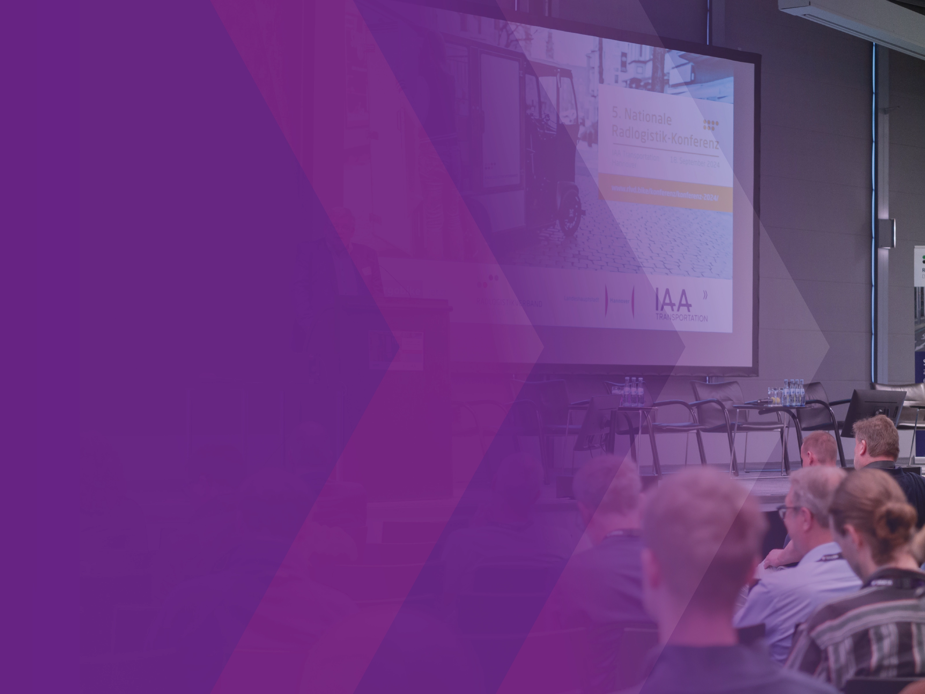 Audience seated before a stage with a presentation screen at a logistics conference.