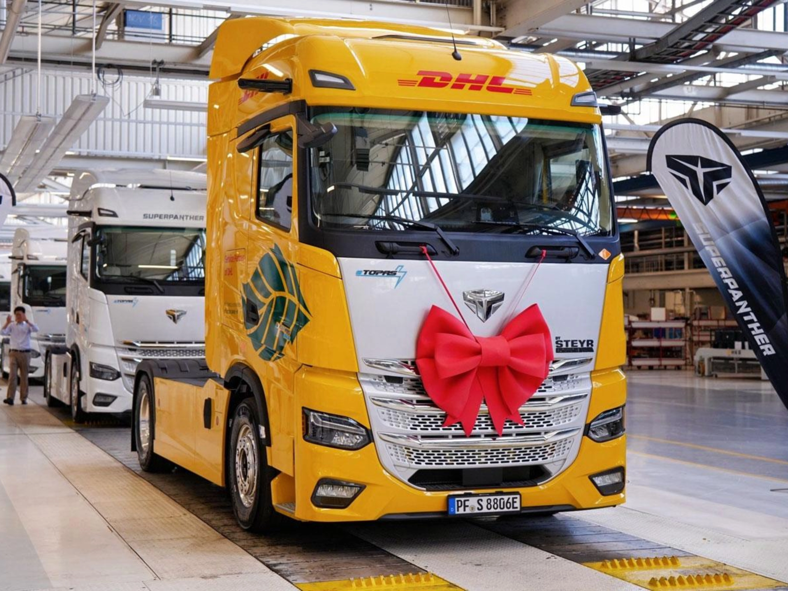 DHL electric truck with a red gift bow displayed inside a production hall.