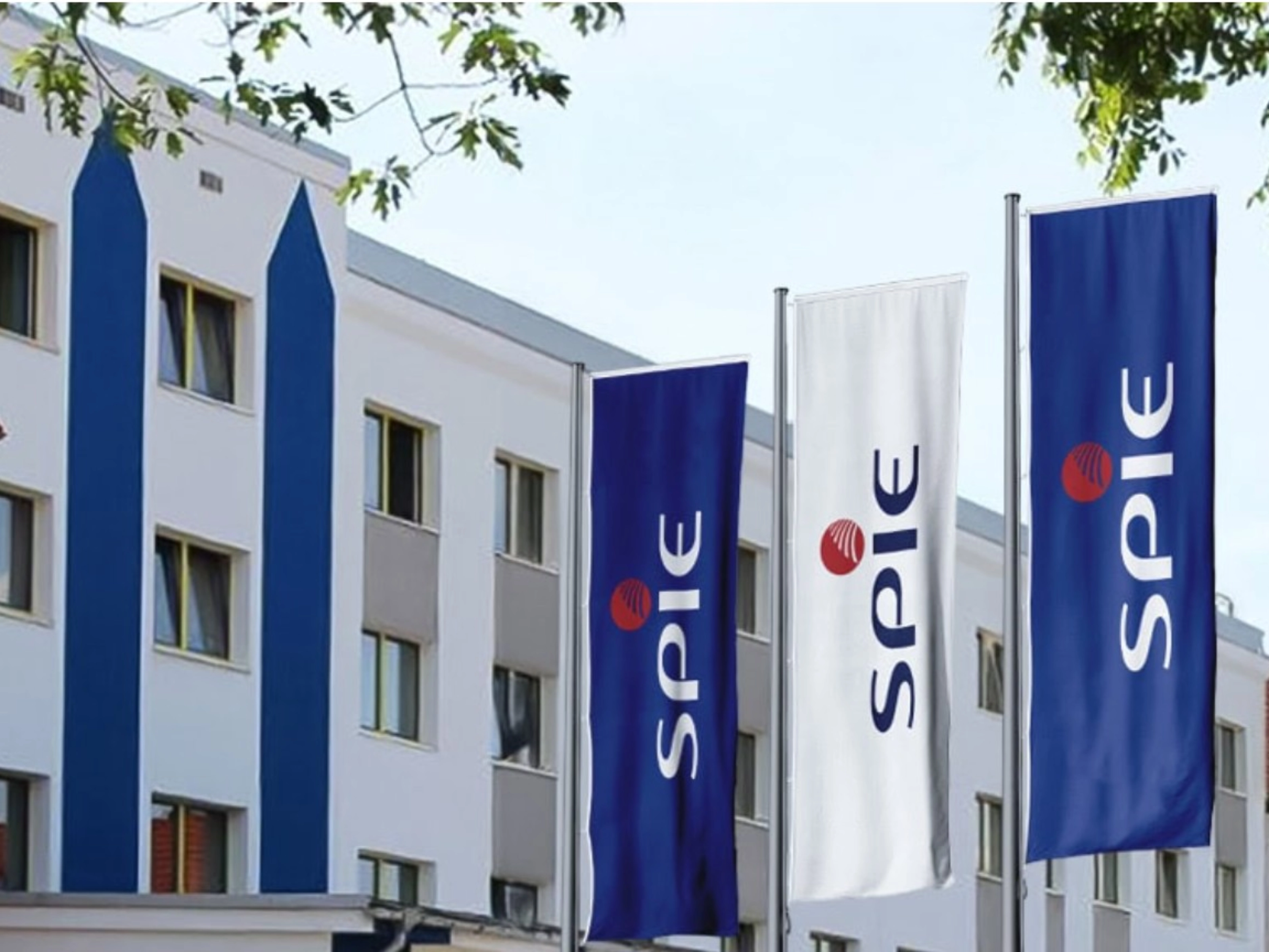 SPIE-Gebäude mit mehreren blauen SPIE-Flaggen an der Fassade.