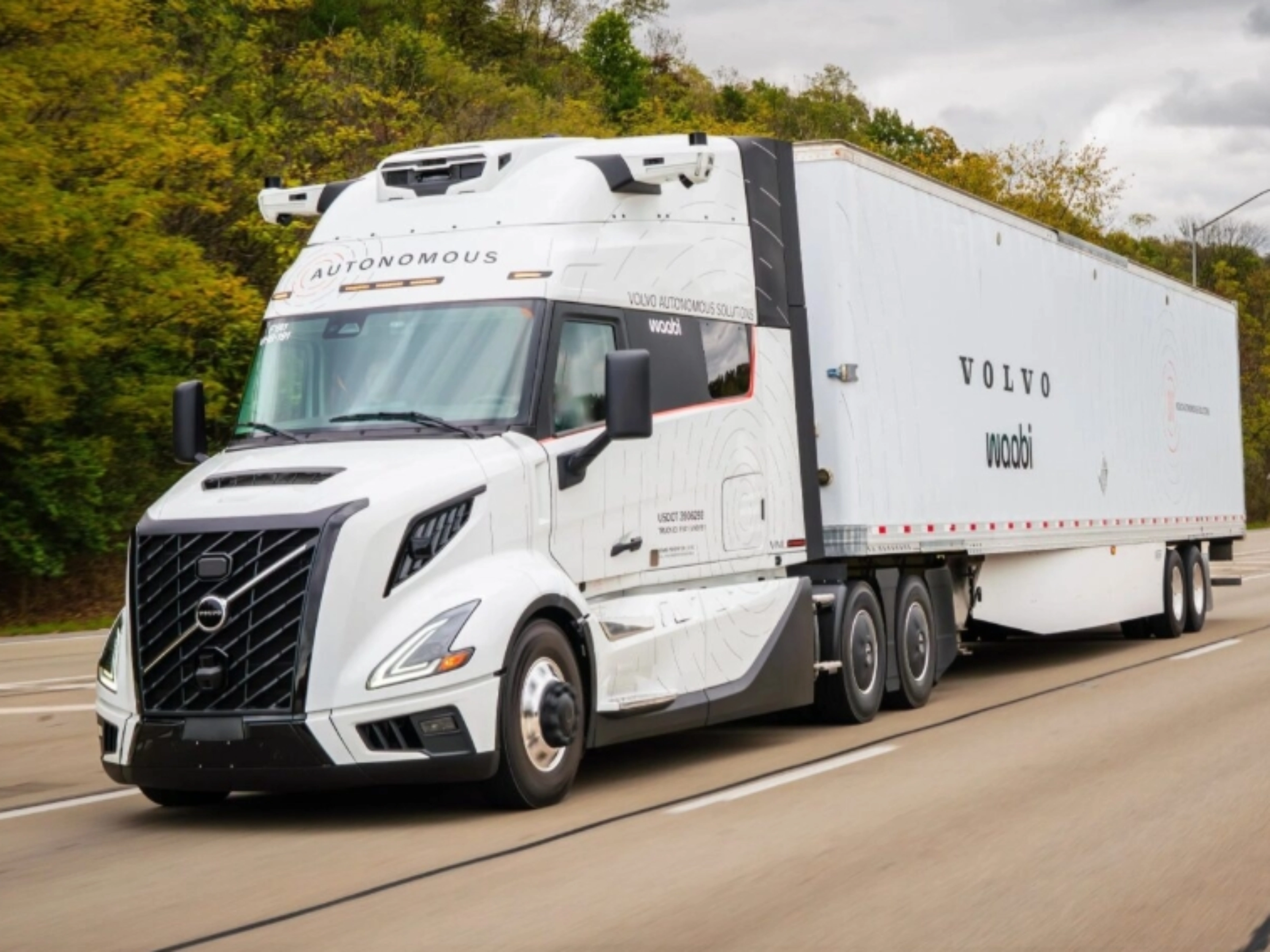 Ein weißer autonomer Volvo-Lkw mit Waabi-Logo fährt auf einer Autobahn an Bäumen vorbei.