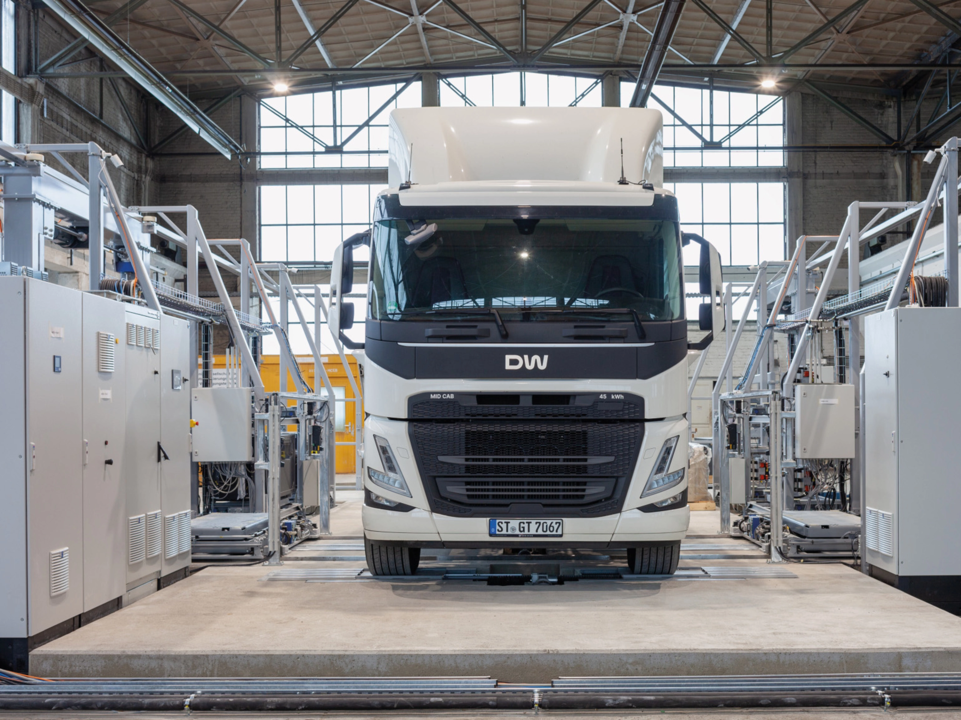 Electric truck in a test hall, surrounded by technical equipment and control cabinets.