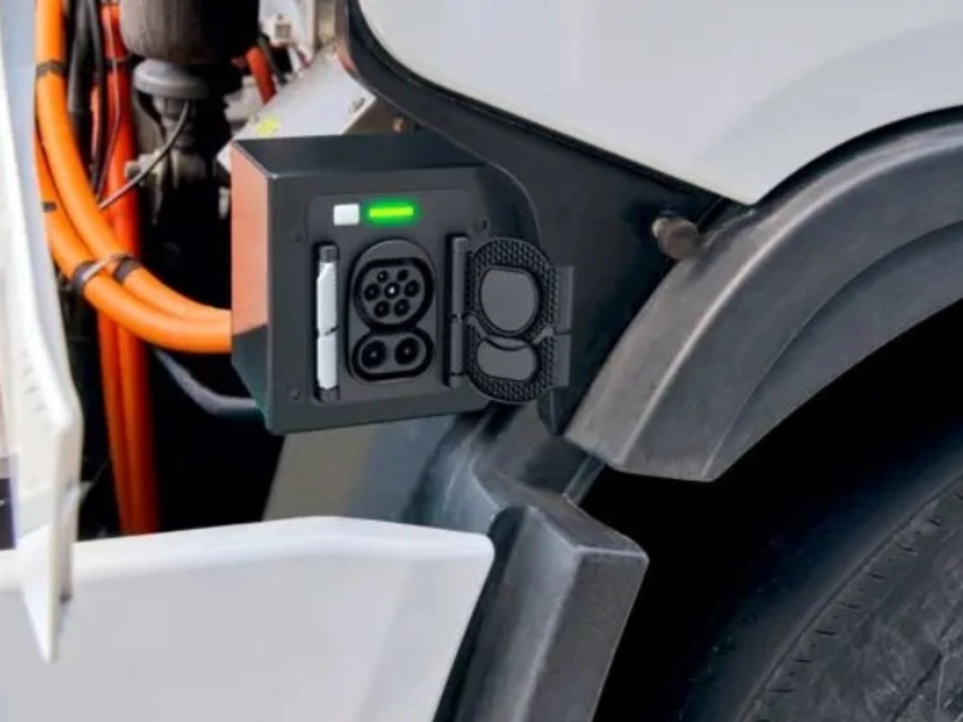 Charging port of an electric truck with visible high-voltage cables and a green status light.