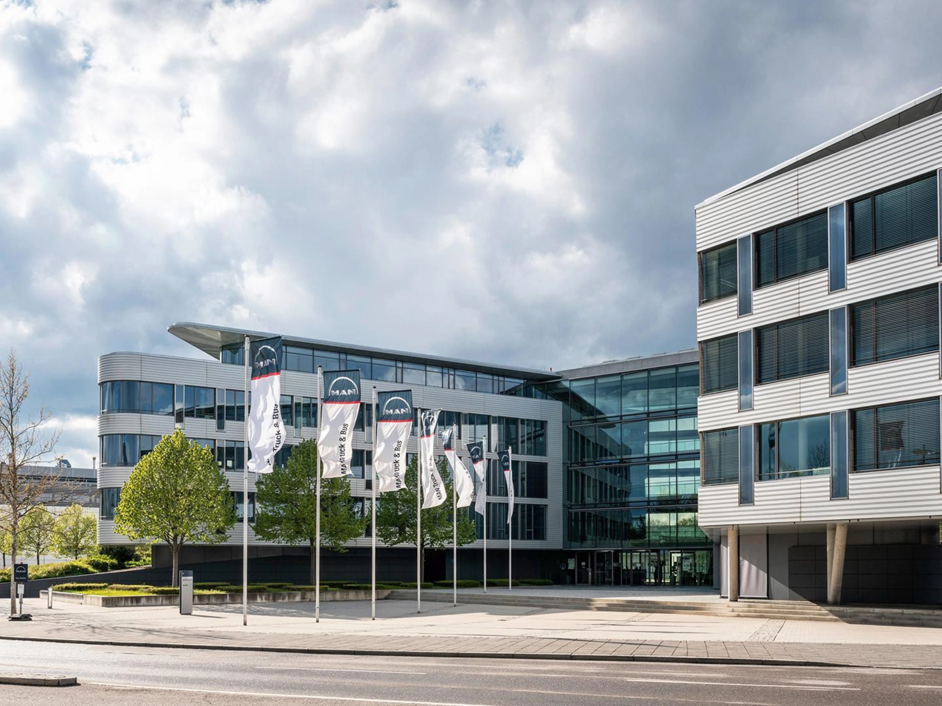 Modern office building with glass facade and MAN Truck & Bus flags in front.