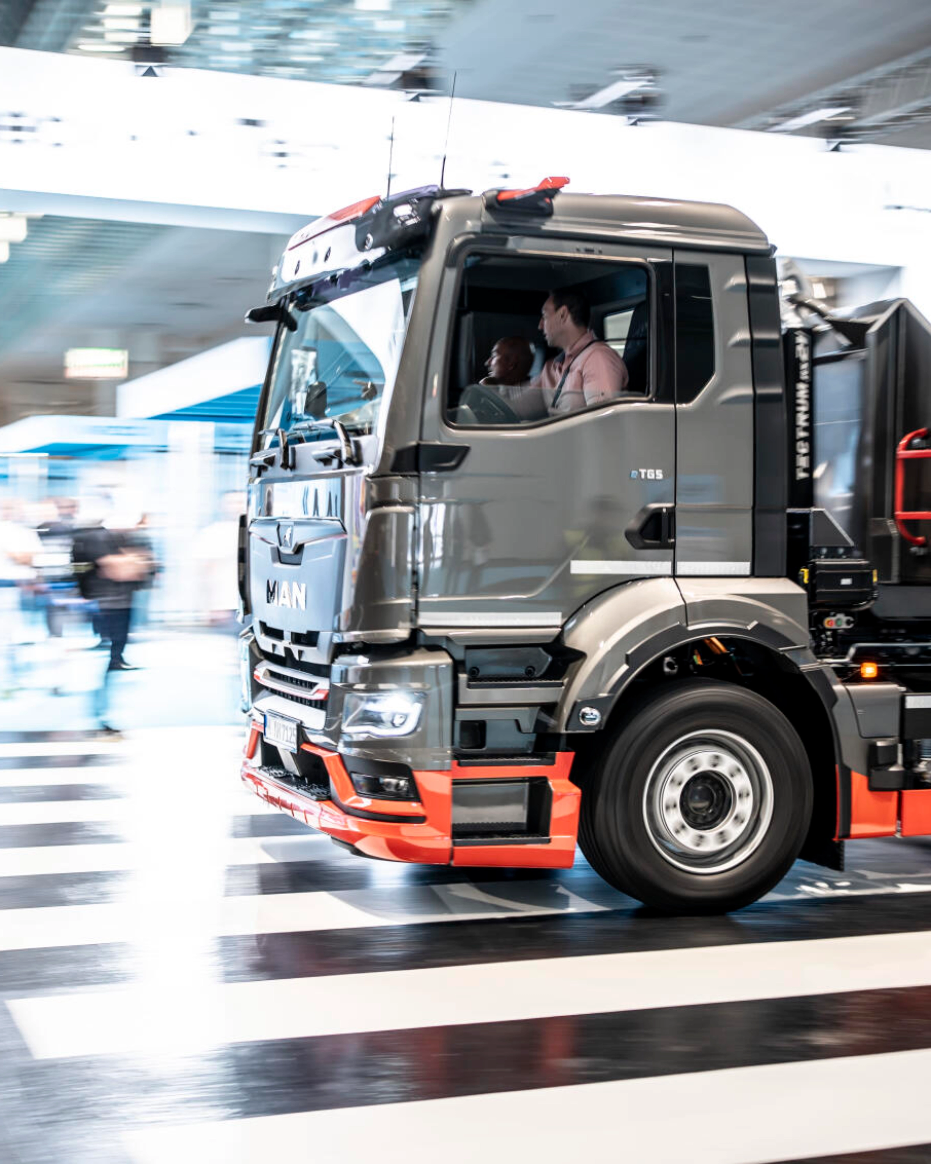 Ein MAN-Lkw fährt mit Bewegungsunschärfe durch ein Testgelände in einer Halle und überquert einen Zebrastreifen.