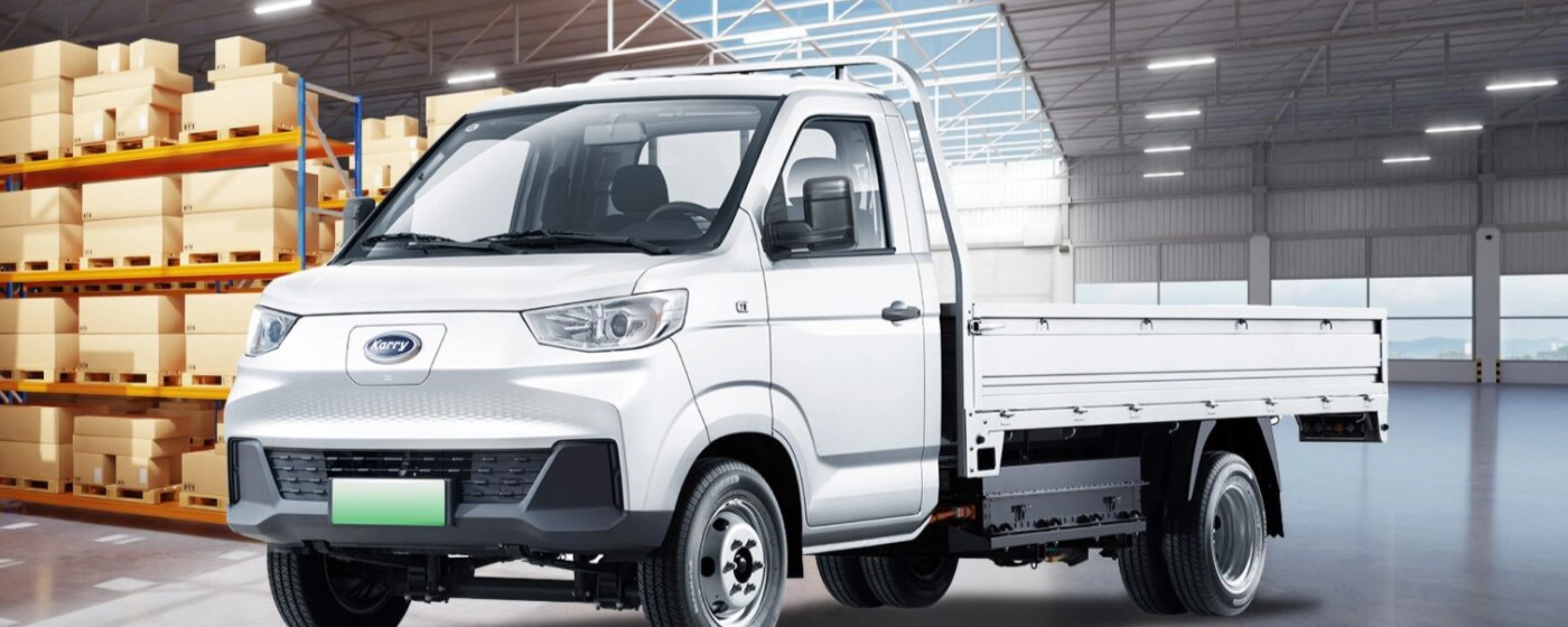 A white Karry electric flatbed truck is parked inside a warehouse near stacked boxes.