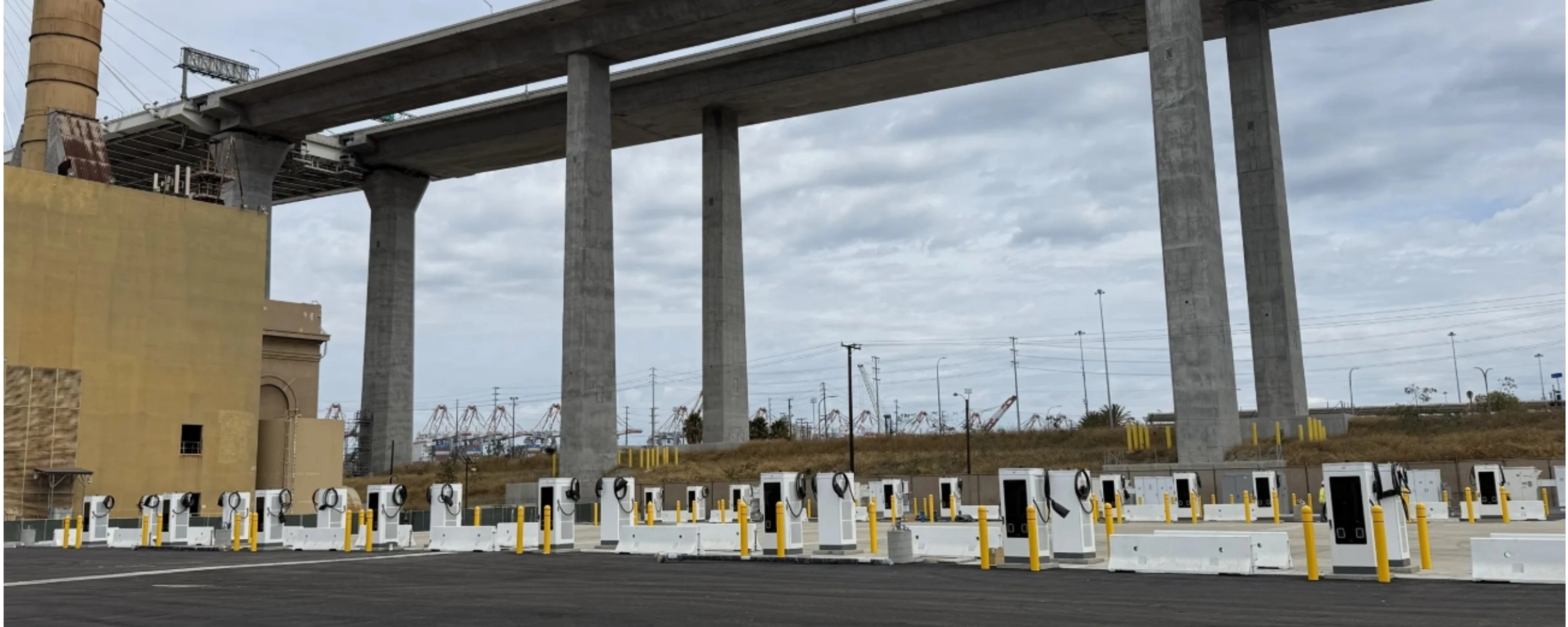 Mehrere E-Ladestationen auf einem Parkplatz unter einer Autobahnbrücke.