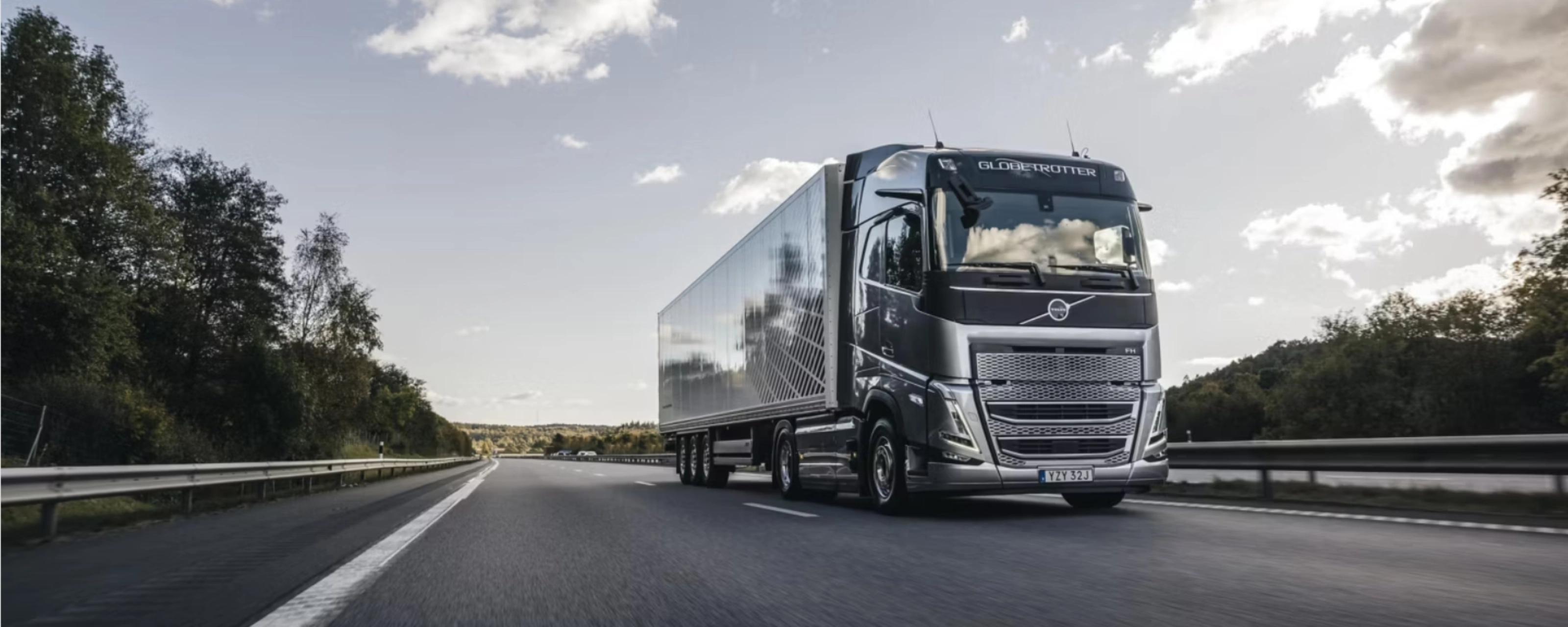 Ein moderner Volvo-Lkw fährt auf einer von Bäumen gesäumten Autobahn unter leicht bewölktem Himmel.