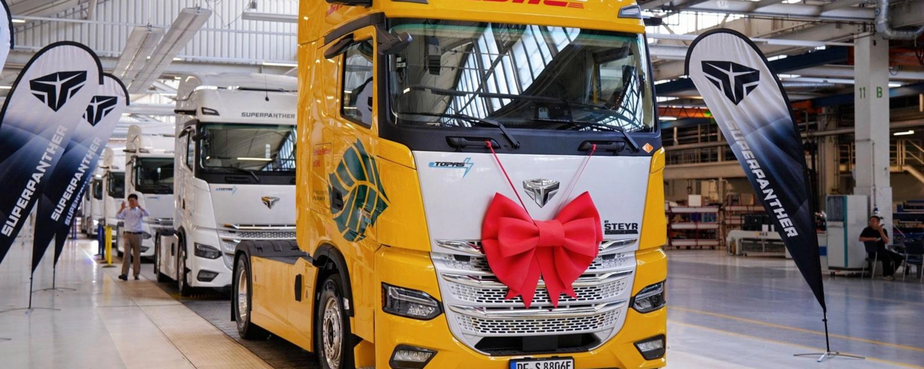 DHL electric truck with a red gift bow displayed inside a production hall.