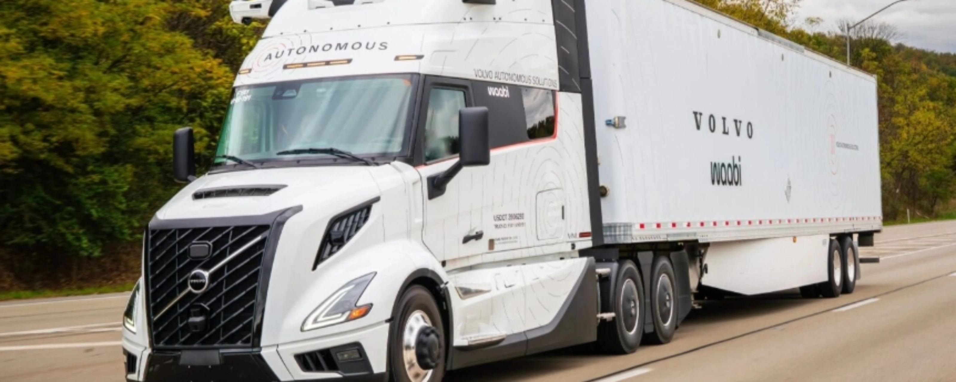 Ein weißer autonomer Volvo-Lkw mit Waabi-Logo fährt auf einer Autobahn an Bäumen vorbei.