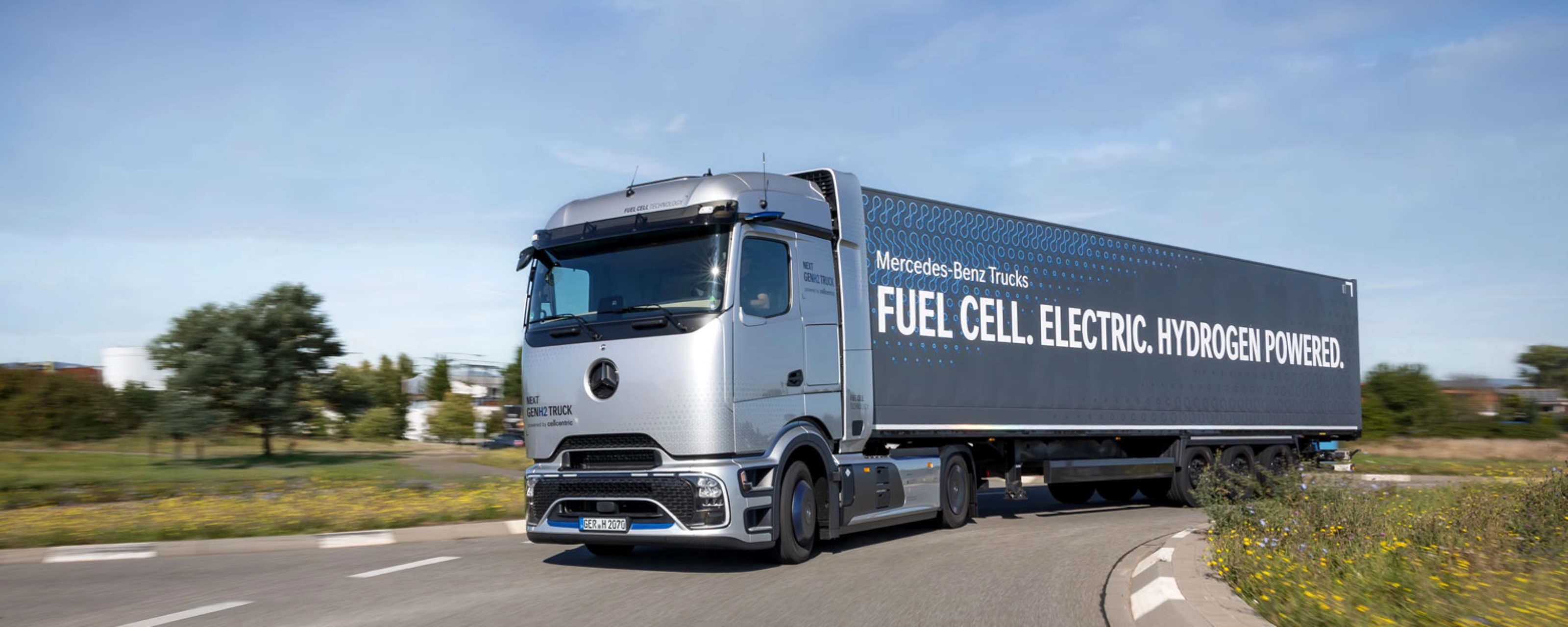 Wasserstoffbetriebener Mercedes-Lkw fährt auf einer kurvigen Straße im ländlichen Gebiet.
