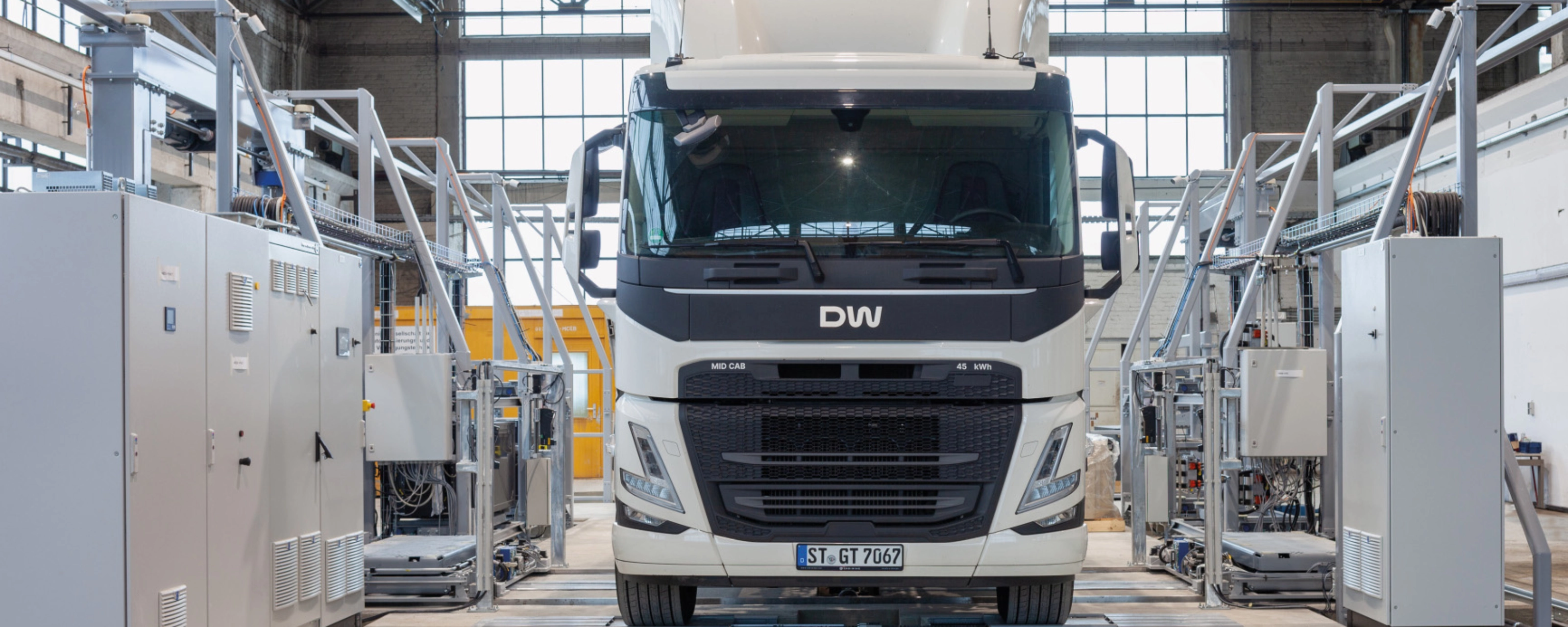 Electric truck in a test hall, surrounded by technical equipment and control cabinets.
