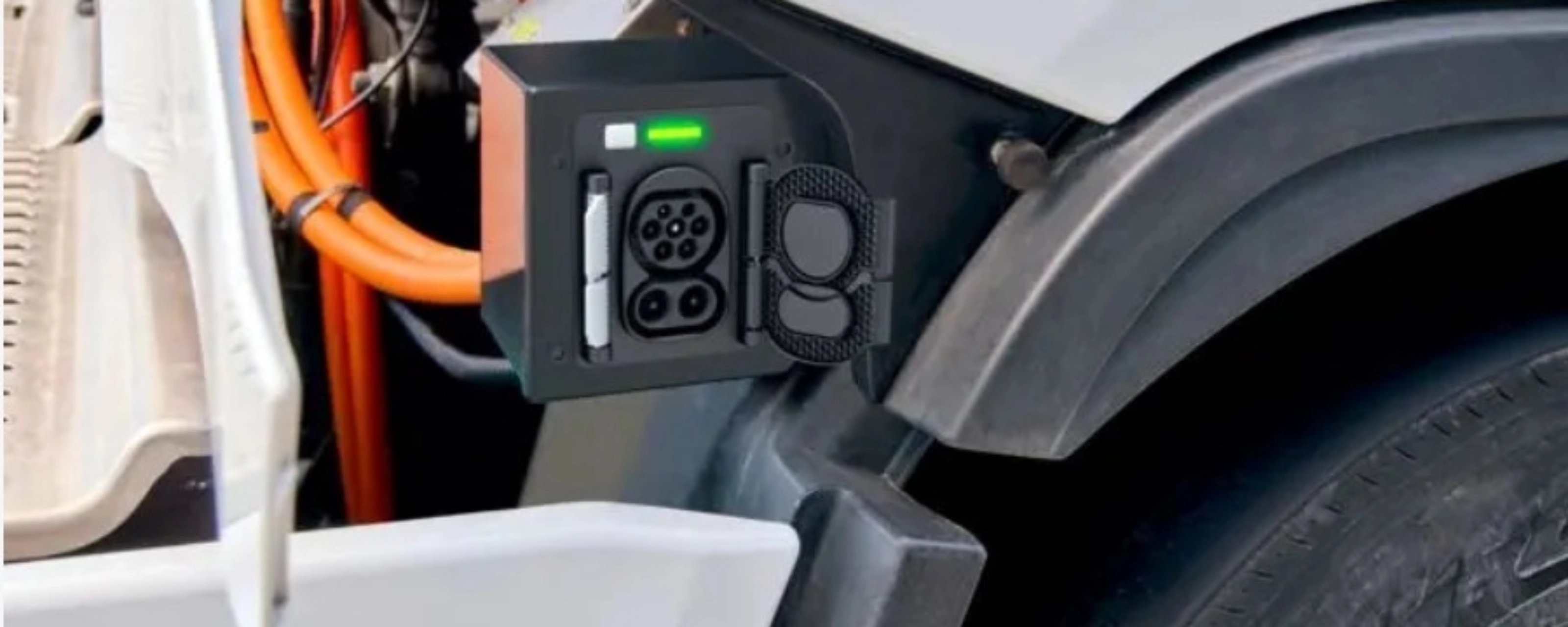 Charging port of an electric truck with visible high-voltage cables and a green status light.