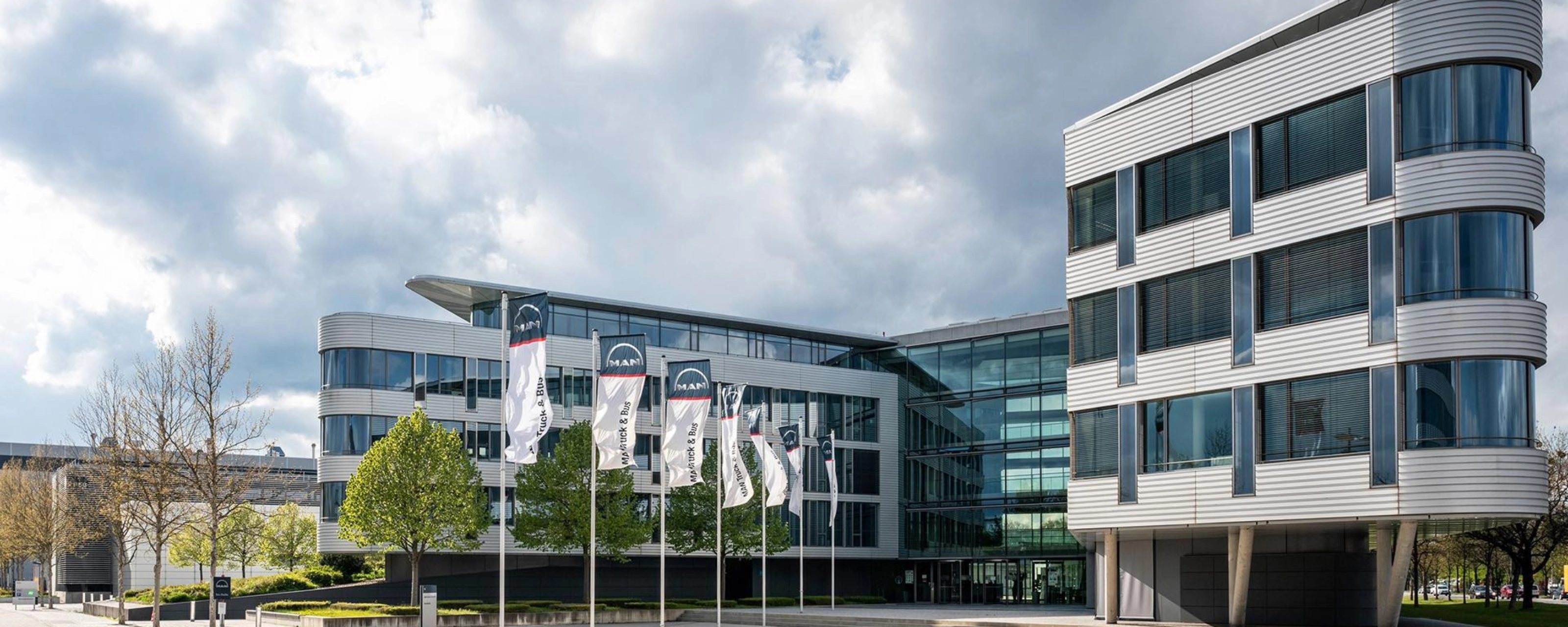 Modern office building with glass facade and MAN Truck & Bus flags in front.