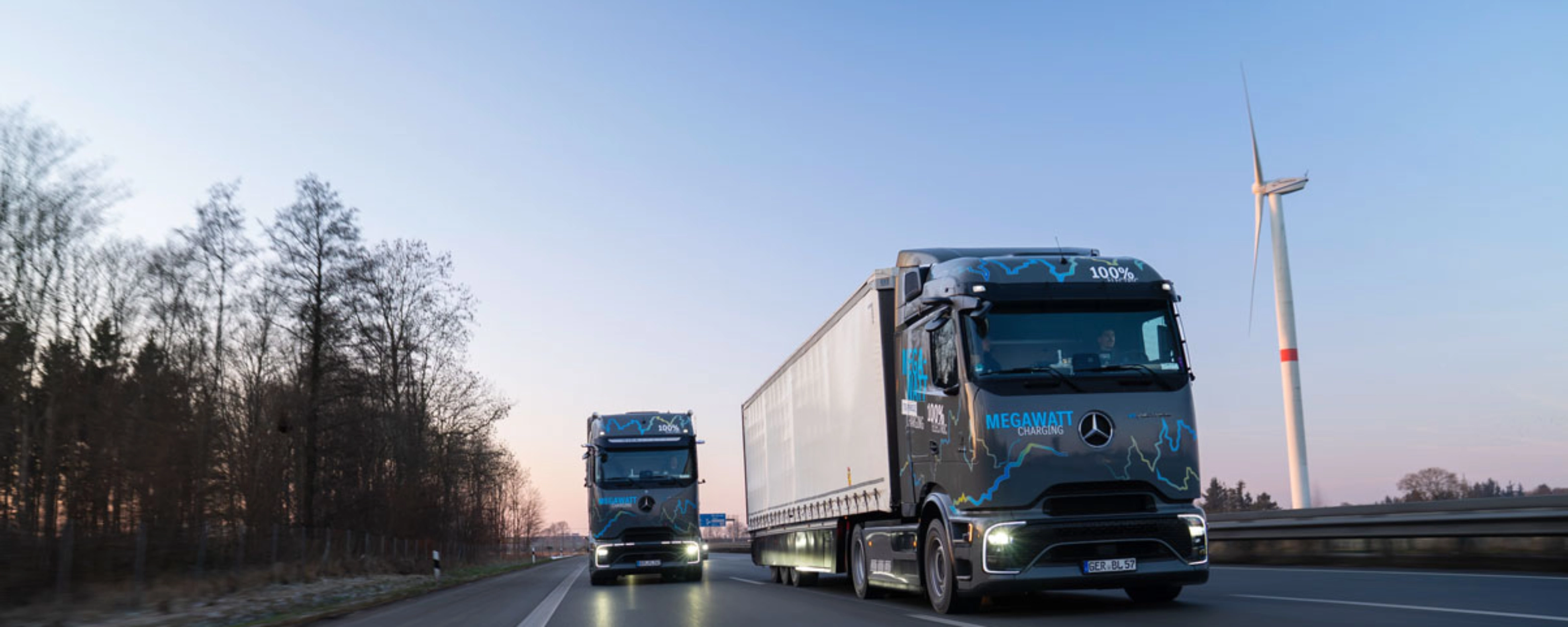 Zwei elektrische Mercedes-Benz-Lkw mit „Megawatt Charging“-Aufschrift fahren bei Dämmerung auf der Autobahn.