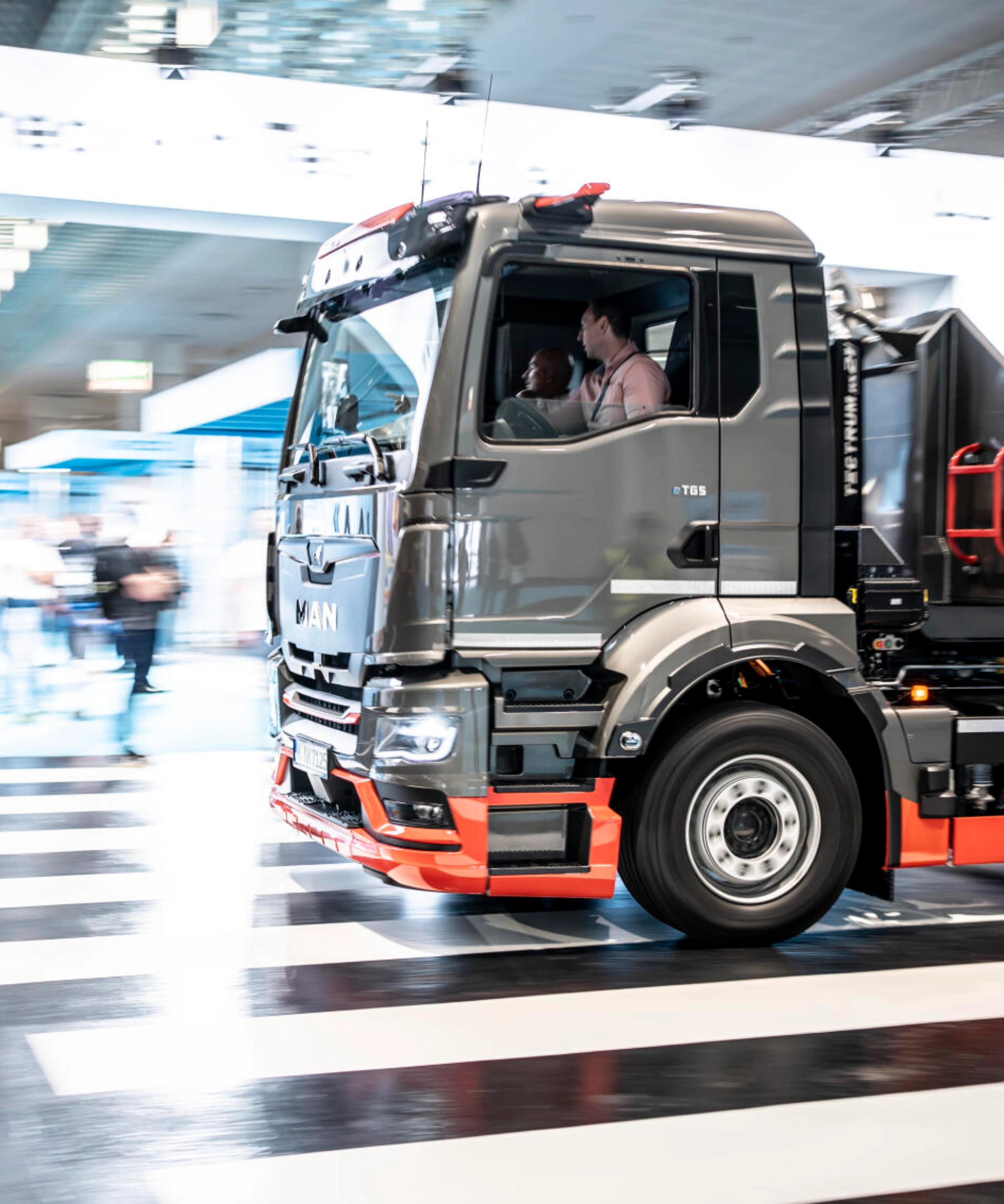 Ein MAN-Lkw fährt mit Bewegungsunschärfe durch ein Testgelände in einer Halle und überquert einen Zebrastreifen.