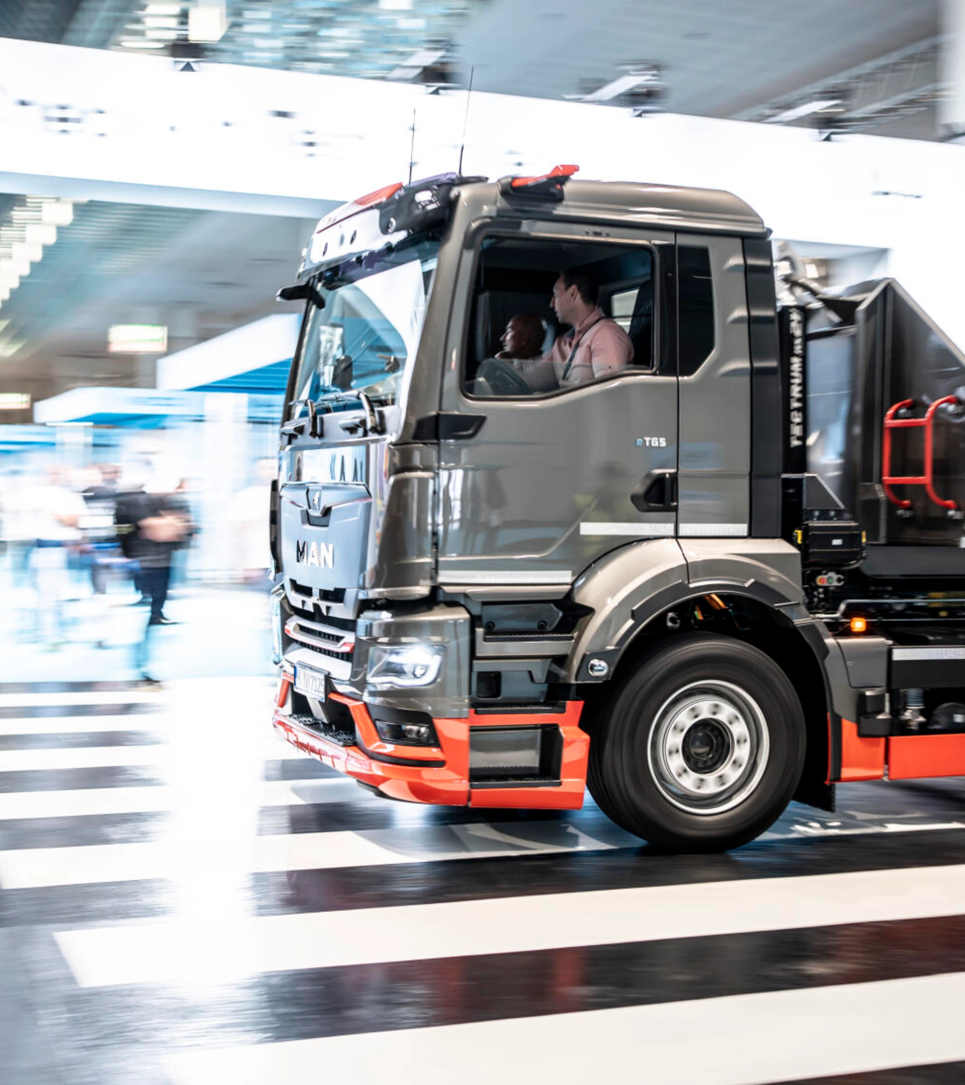Ein MAN-Lkw fährt mit Bewegungsunschärfe durch ein Testgelände in einer Halle und überquert einen Zebrastreifen.