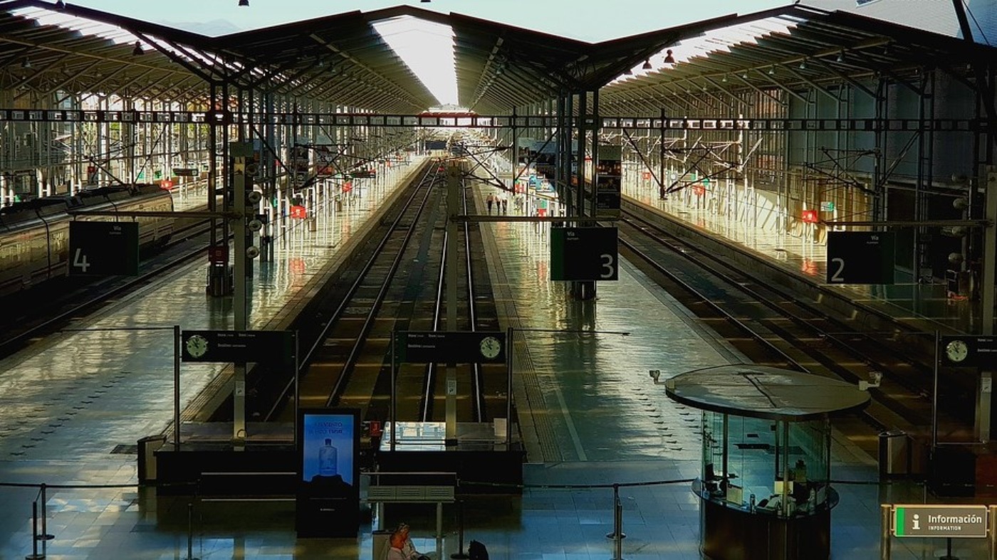Large train station hall with multiple empty tracks and sunlight shining through the roof.