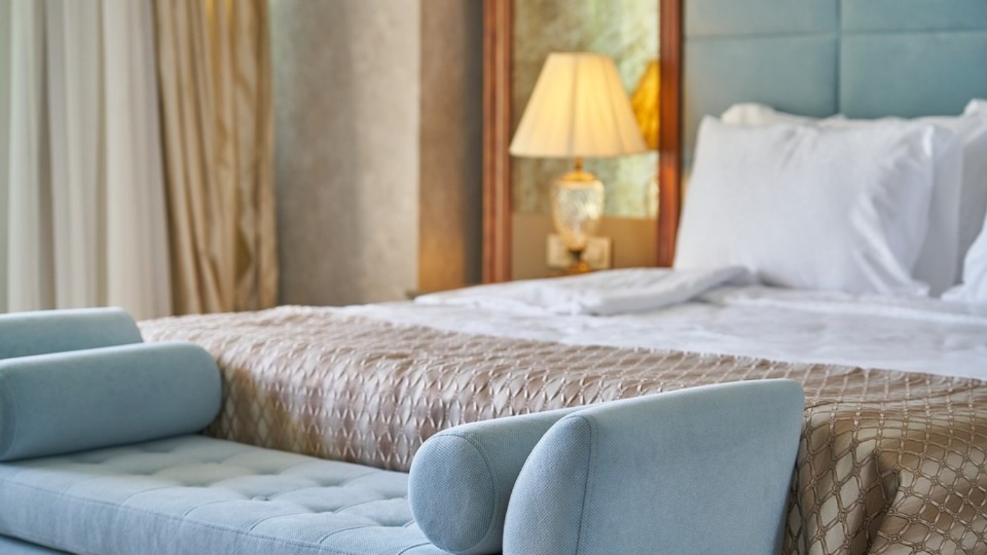 Cozy hotel room with a made bed, a bench at the foot, and a lit bedside lamp.