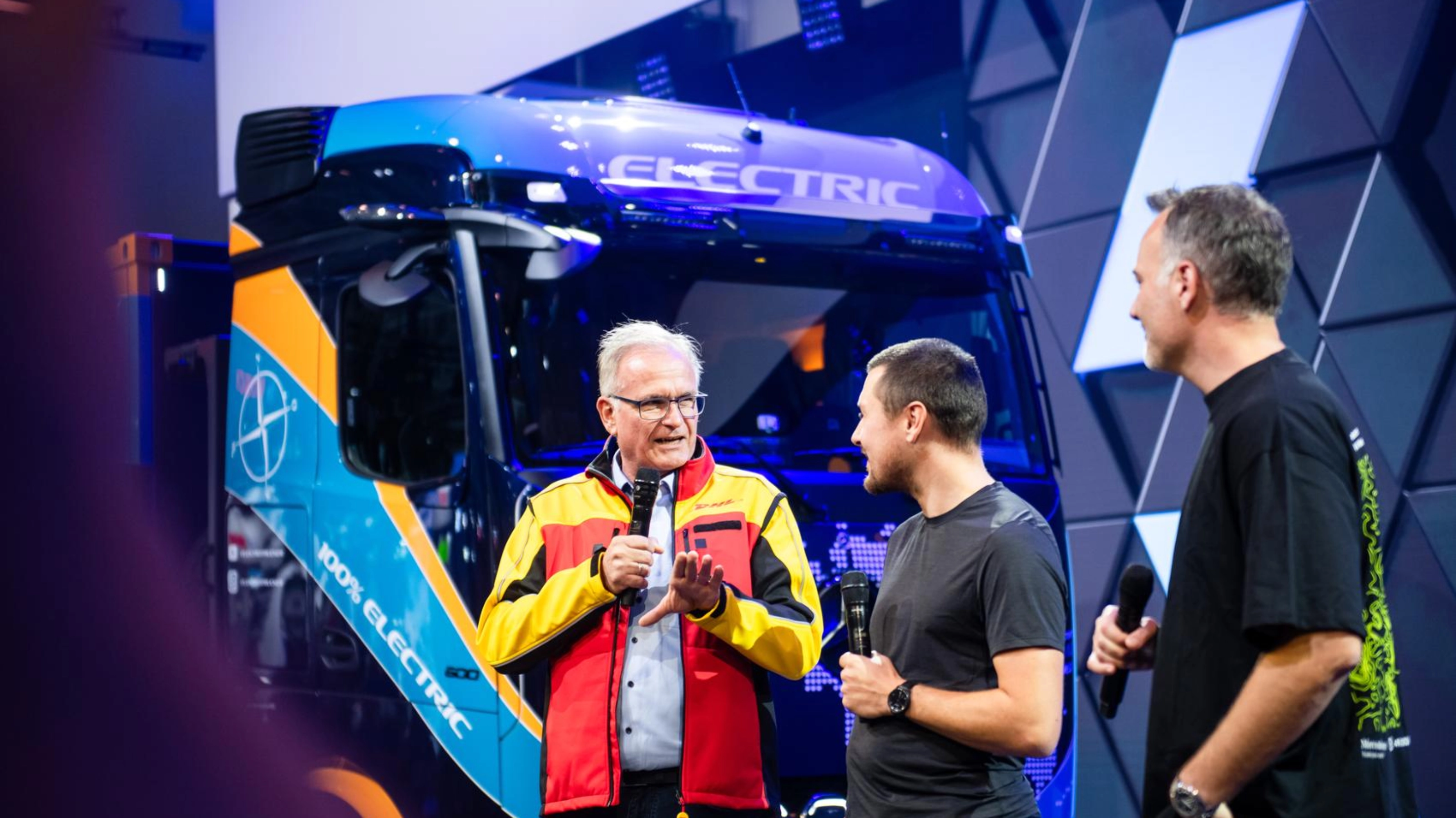 Three men presenting an electric bus on an exhibition stage.