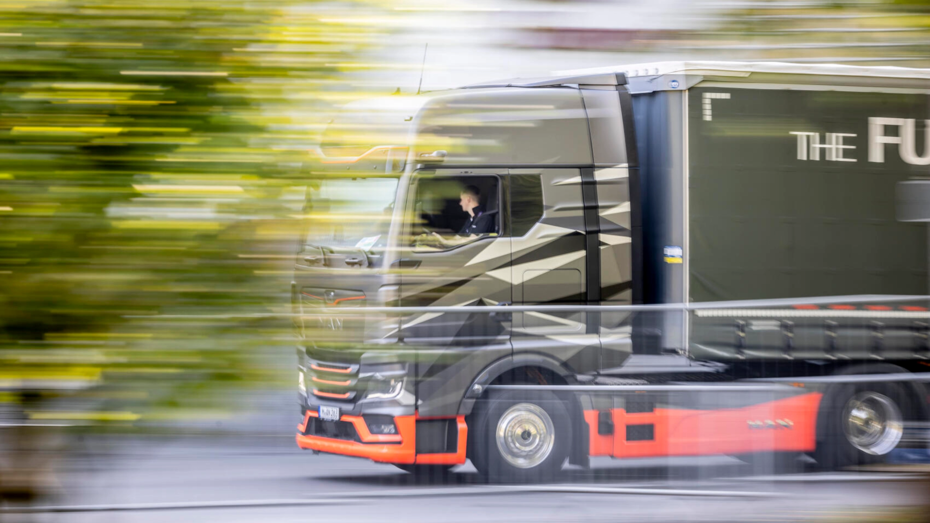 Ein moderner Lkw fährt bei einer Testfahrt im Freien mit hoher Geschwindigkeit vorbei, sichtbar in Bewegungsunschärfe.