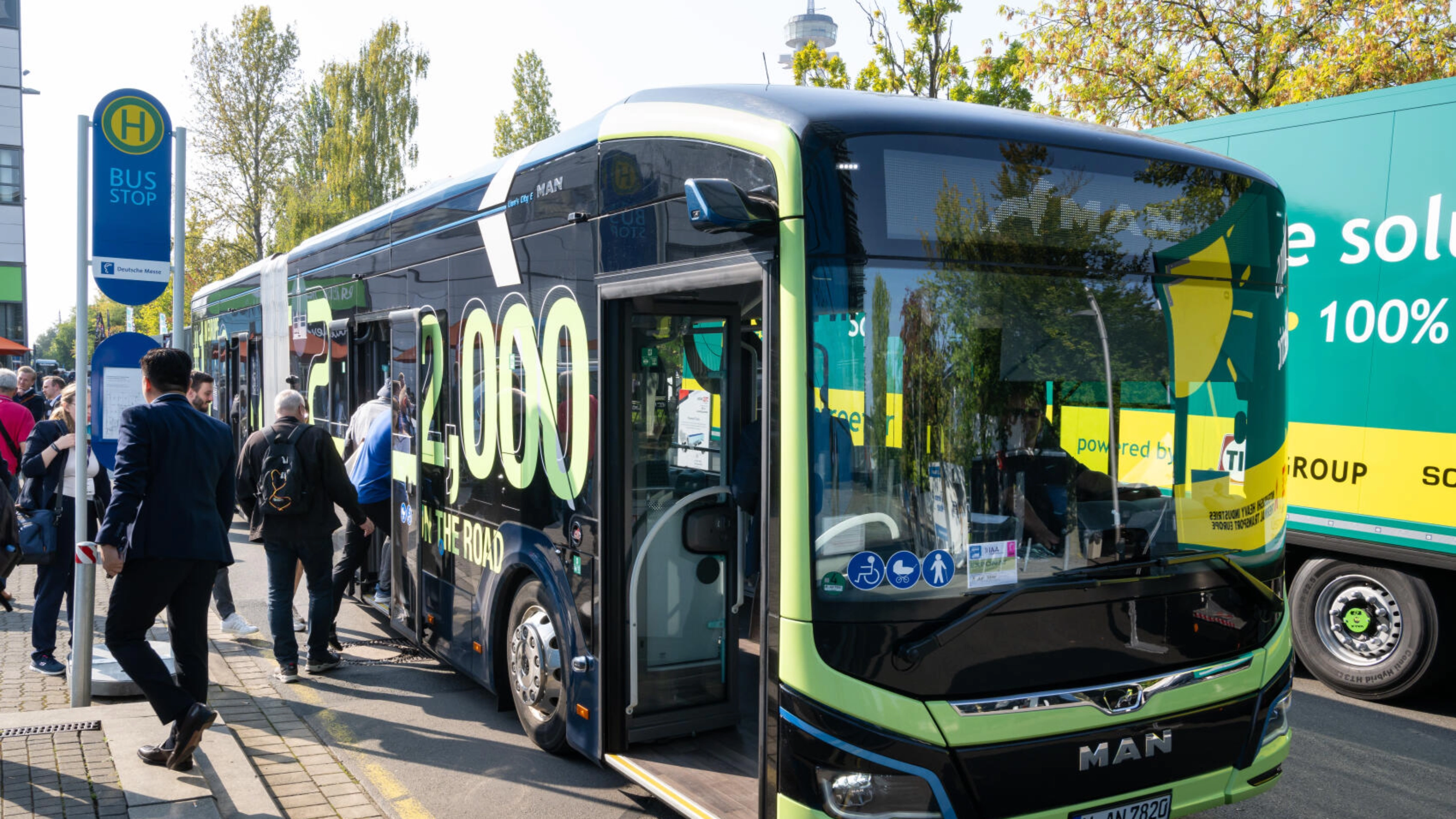 Menschen steigen bei der IAA Transportation an einer Haltestelle in einen modernen MAN-Shuttlebus ein.