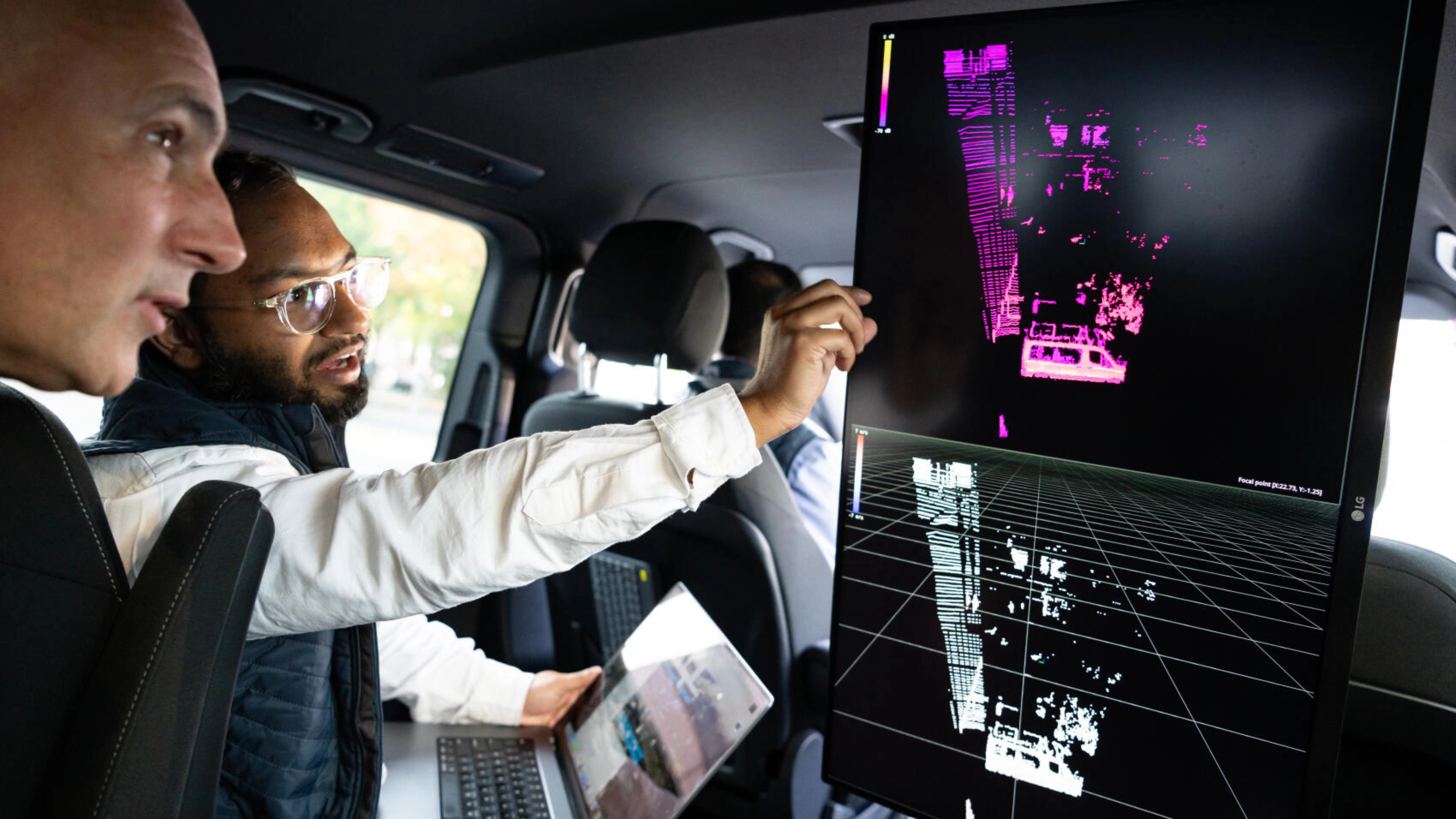 Zwei Männer analysieren Fahrzeugsensordaten auf großem Bildschirm im Auto