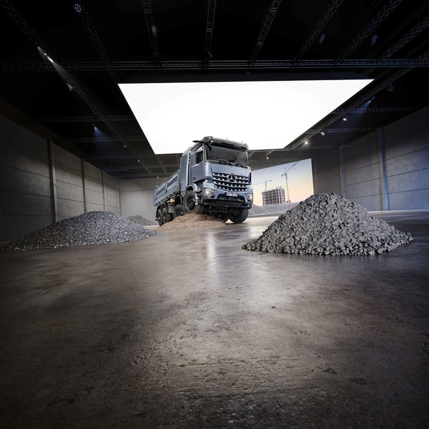 Mercedes-Benz Kipper fährt über Kieshaufen in einer großen Industriehalle mit heller Deckenbeleuchtung.