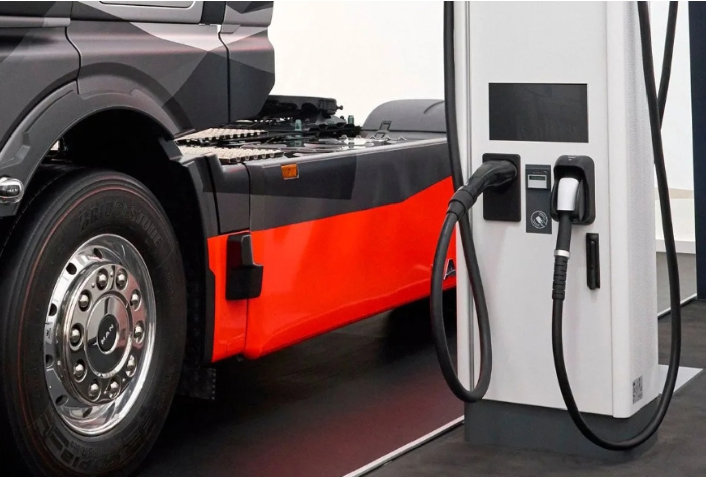 Nahaufnahme eines elektrischen MAN-Lkw beim Laden an einer öffentlichen Ladestation, sichtbar sind Rad, Seitenverkleidung und Ladestecker.
